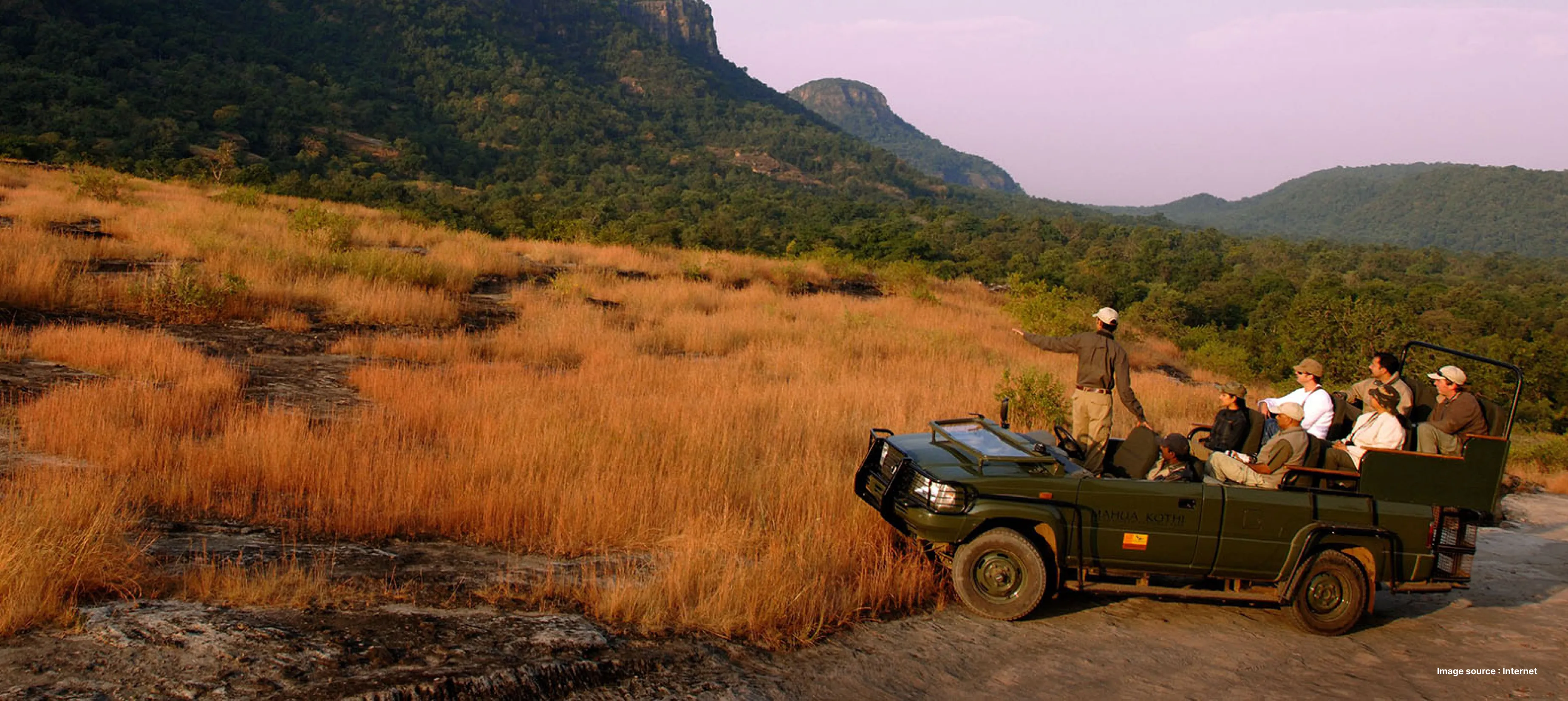a naturalist points to something in a jeep with safari tourists close to the bottom of a green hill