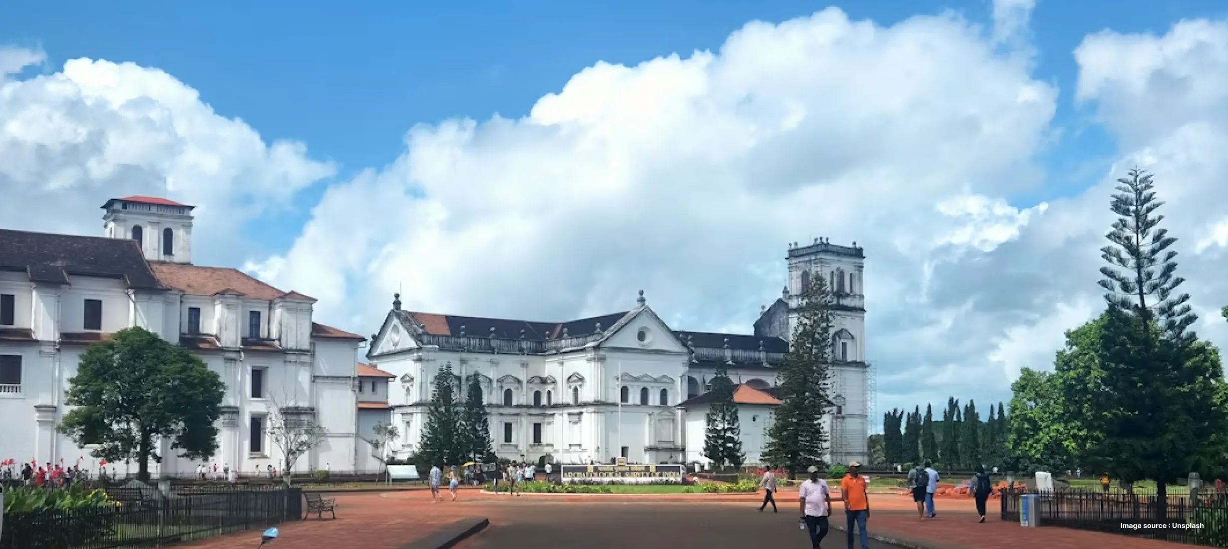 a distant shot of an ancient cathedral in goa on a cloudy day with tourists walking by