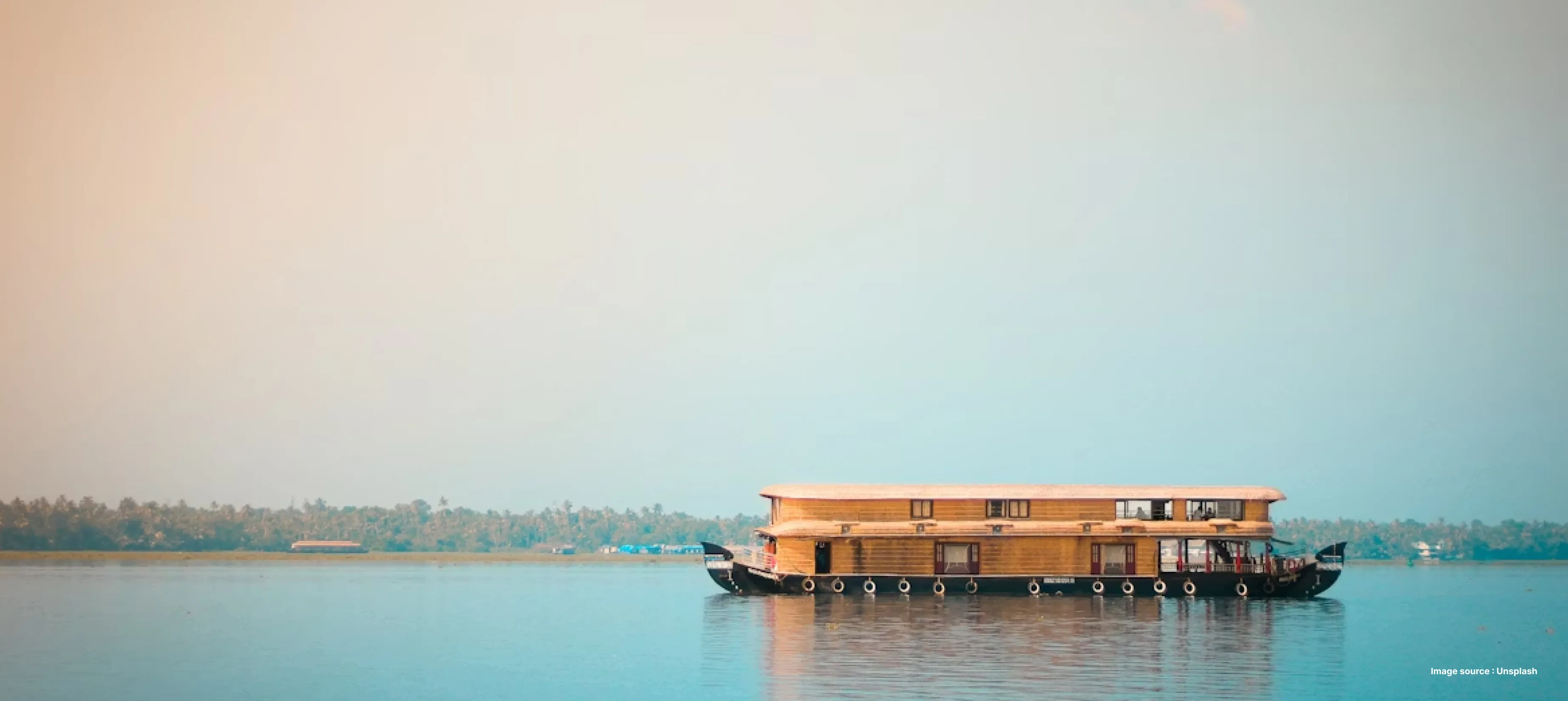 a side view of a wooden houseboat cruising backwaters in kerala during sunset