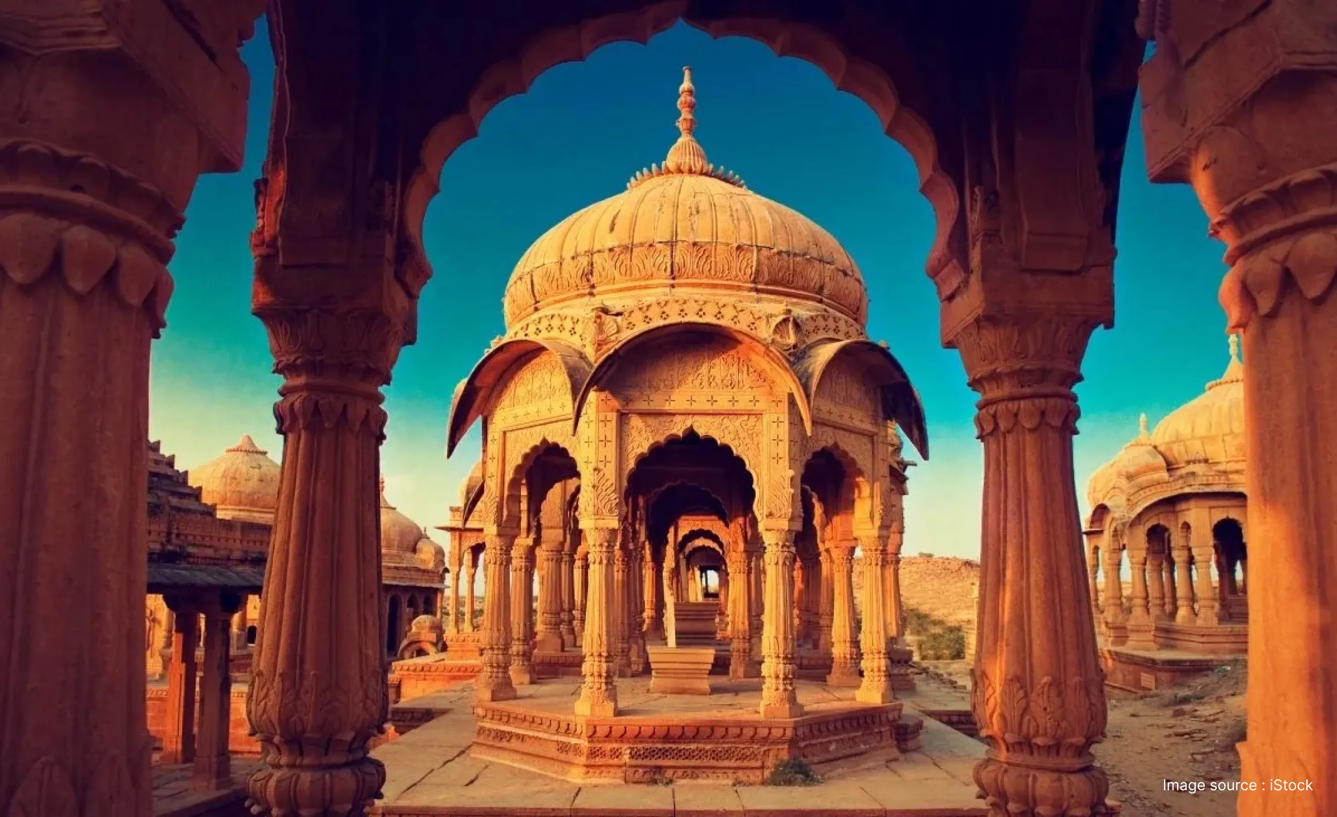 Ornate golden sandstone cenotaphs at Bada Bagh seen through a stone archway during sunset in Jaisalmer.