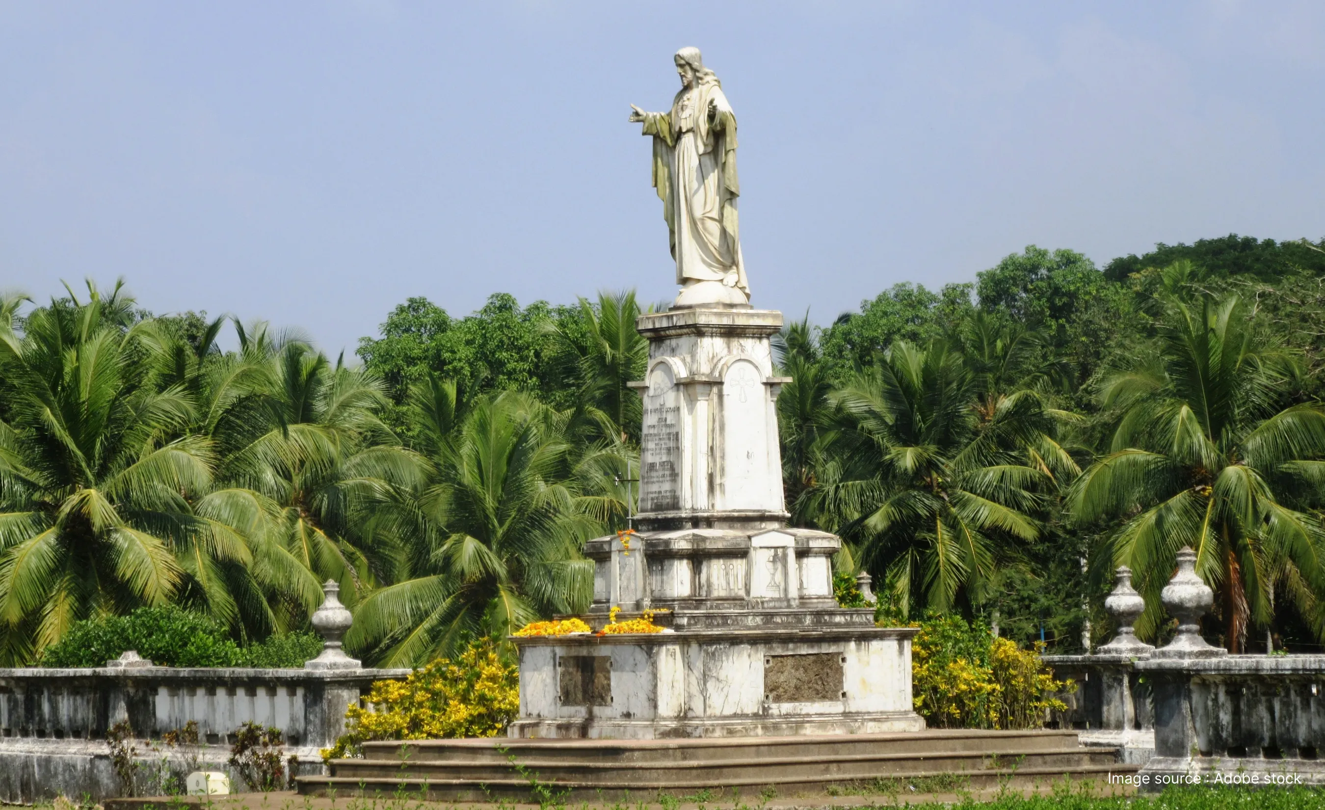 Sacred Heart of Jesus statue in Old Goa standing atop a marble pedestal, surrounded by lush palm trees and greenery