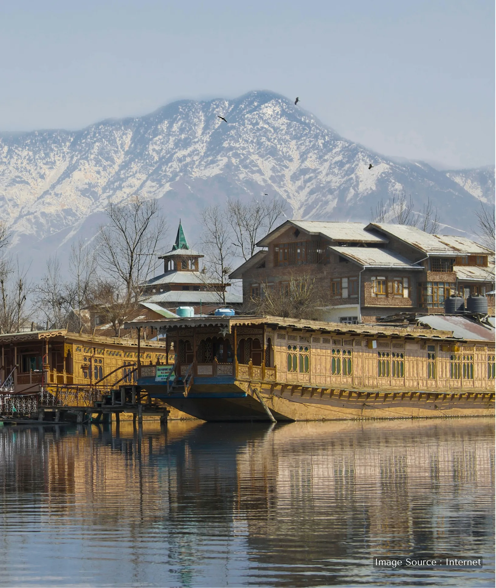 Traditional hand-carved wooden houseboats on Dal Lake, Srinagar, with snow-capped Himalayan peaks and local architecture in the background.