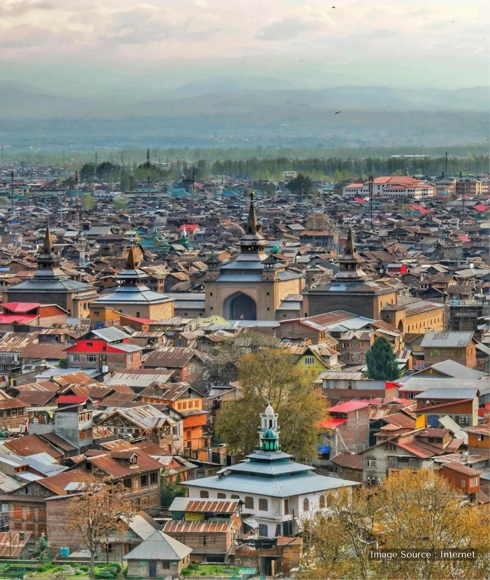 Aerial view of the Old City in Srinagar, Kashmir, featuring the traditional wooden architecture of Jamia Masjid and dense residential rooftops against a hazy mountain backdrop.
