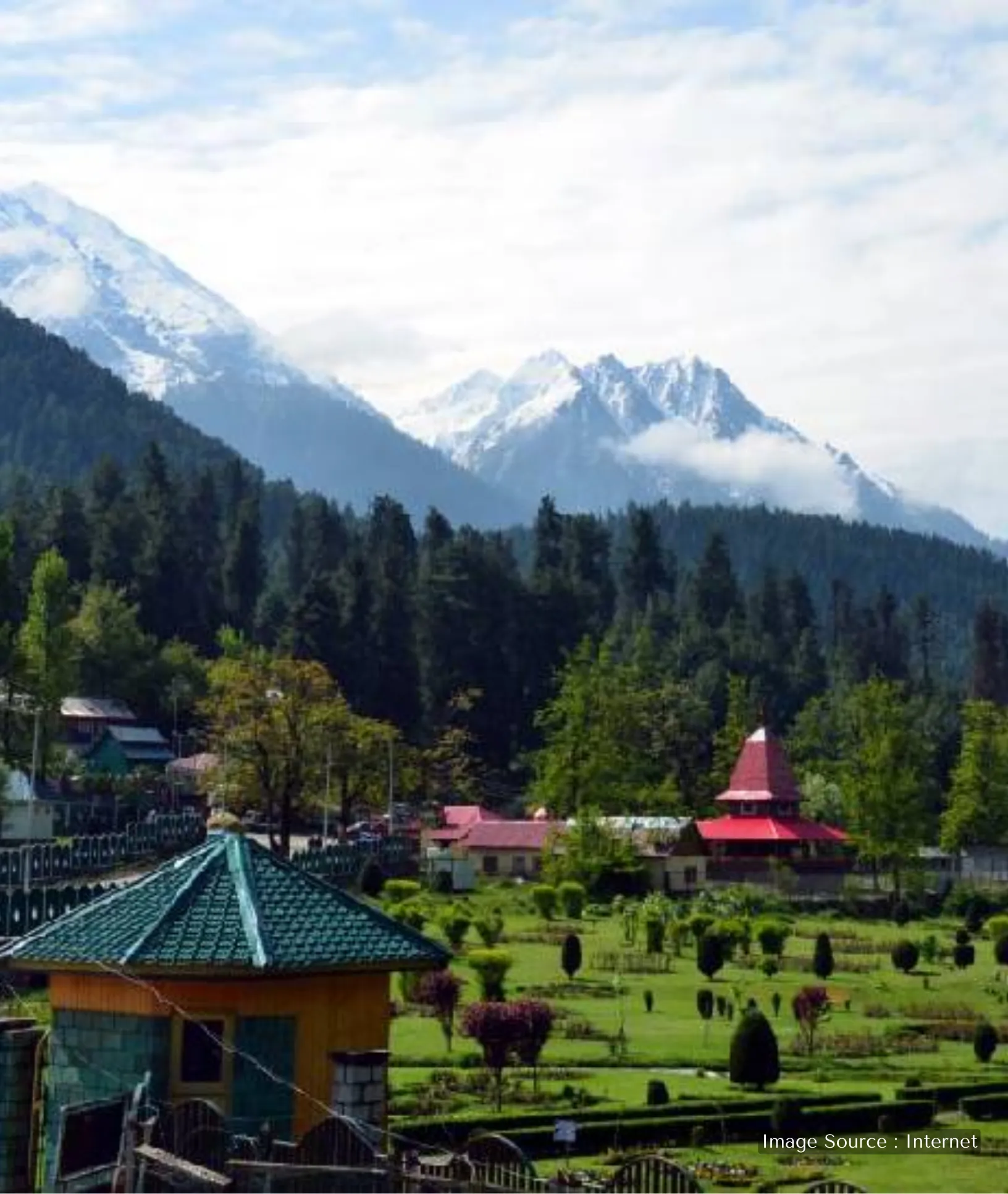 A scenic overlook of Pahalgam valley with a winding asphalt road, dense coniferous forests, and hazy blue mountain peaks.