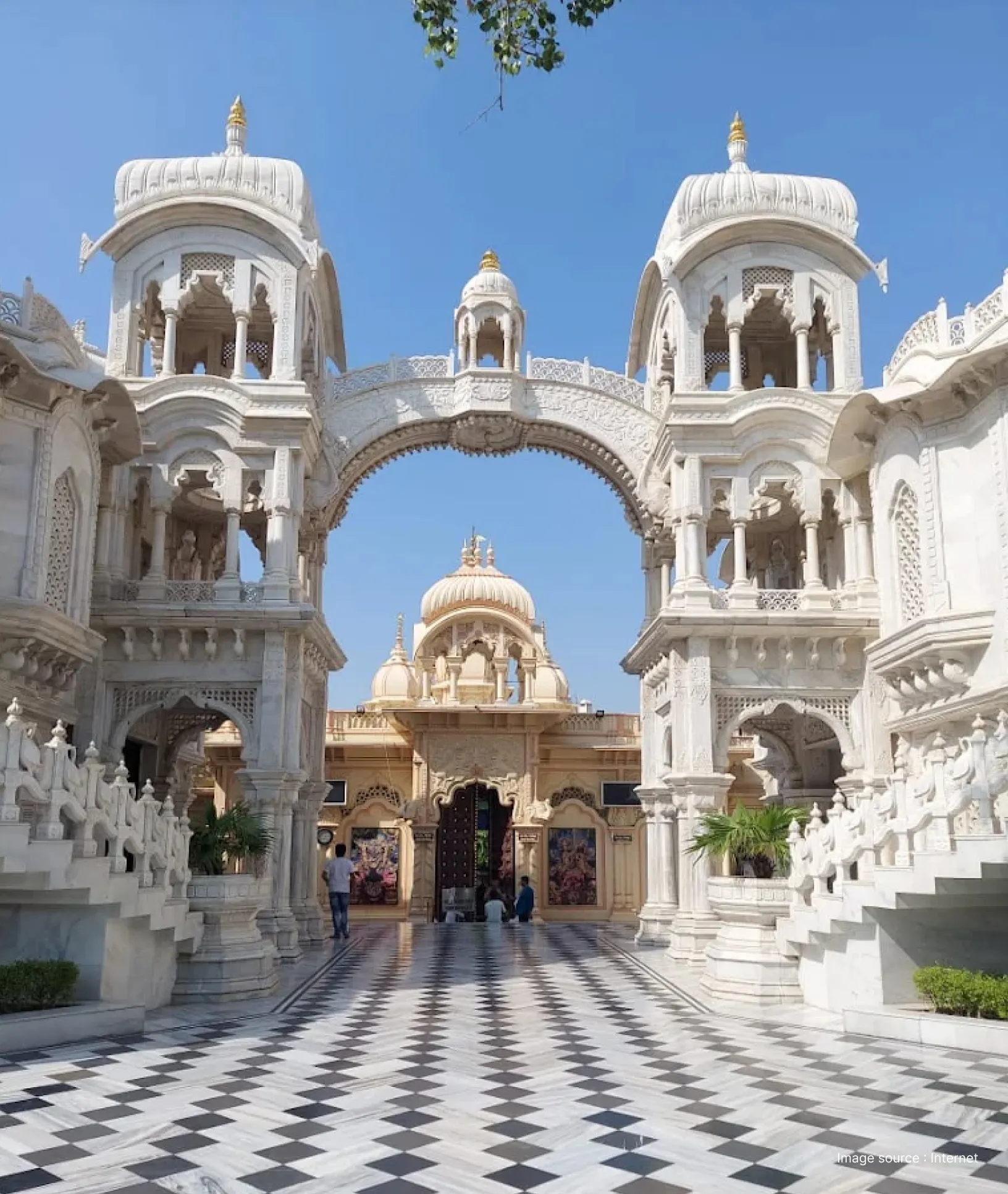 The white marble entrance gate and courtyard of ISKCON Vrindavan (Krishna Balaram Mandir) with a checkerboard floor and ornate arches.