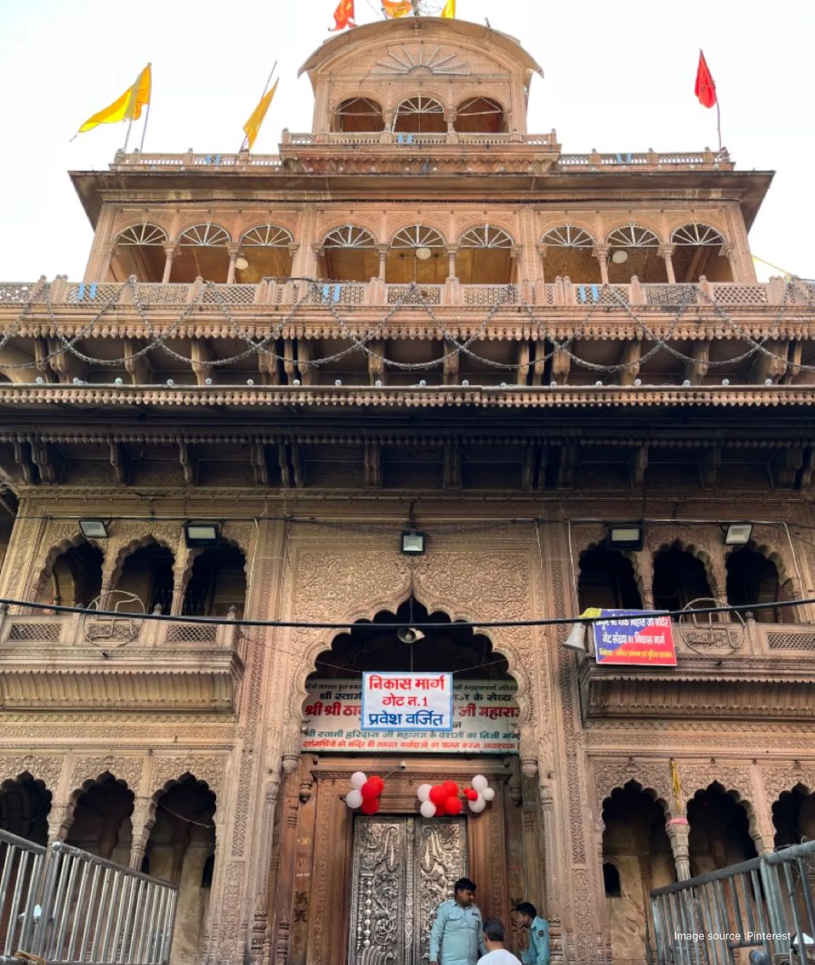 The traditional multi-storied facade and entrance of the Shri Banke Bihari Ji Temple in Vrindavan decorated with yellow and red flags.