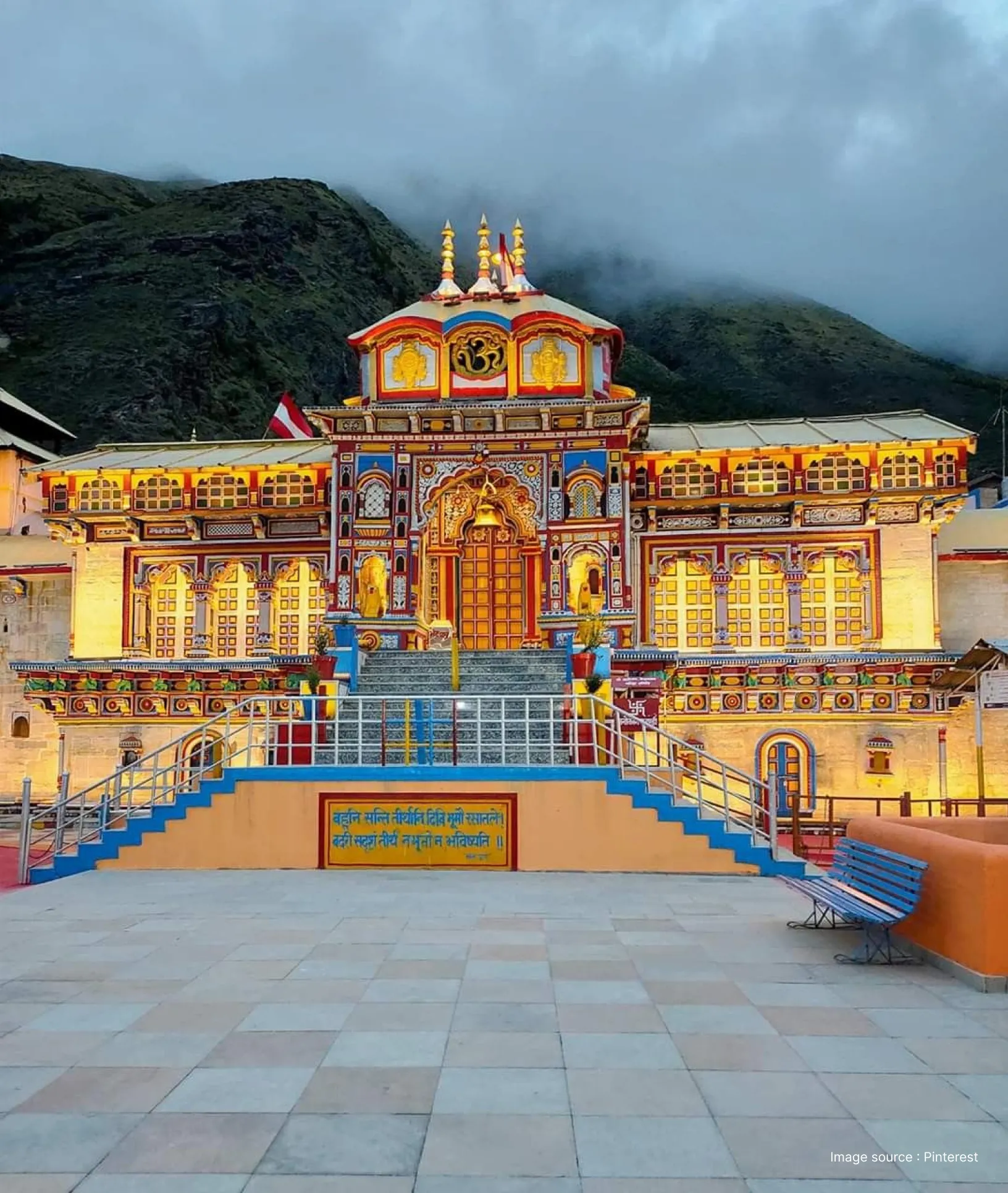 Badrinath Temple in Uttarakhand illuminated at dusk, showcasing its colorful façade, ornate entrance, and Himalayan mountains in the background