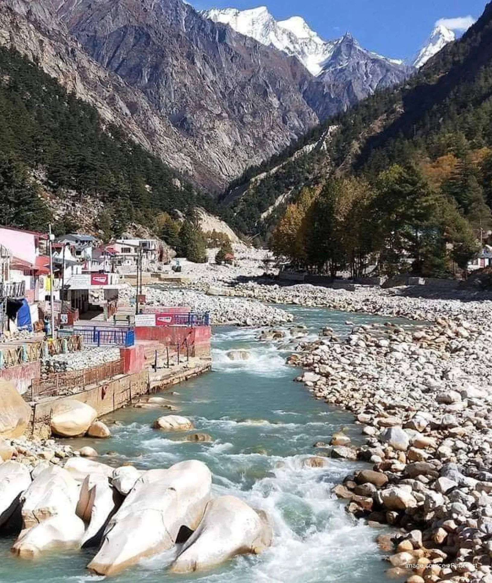 Scenic view of Badrinath city in Uttarakhand with the Alaknanda River flowing through rocky riverbanks, Himalayan mountains, and riverside buildings