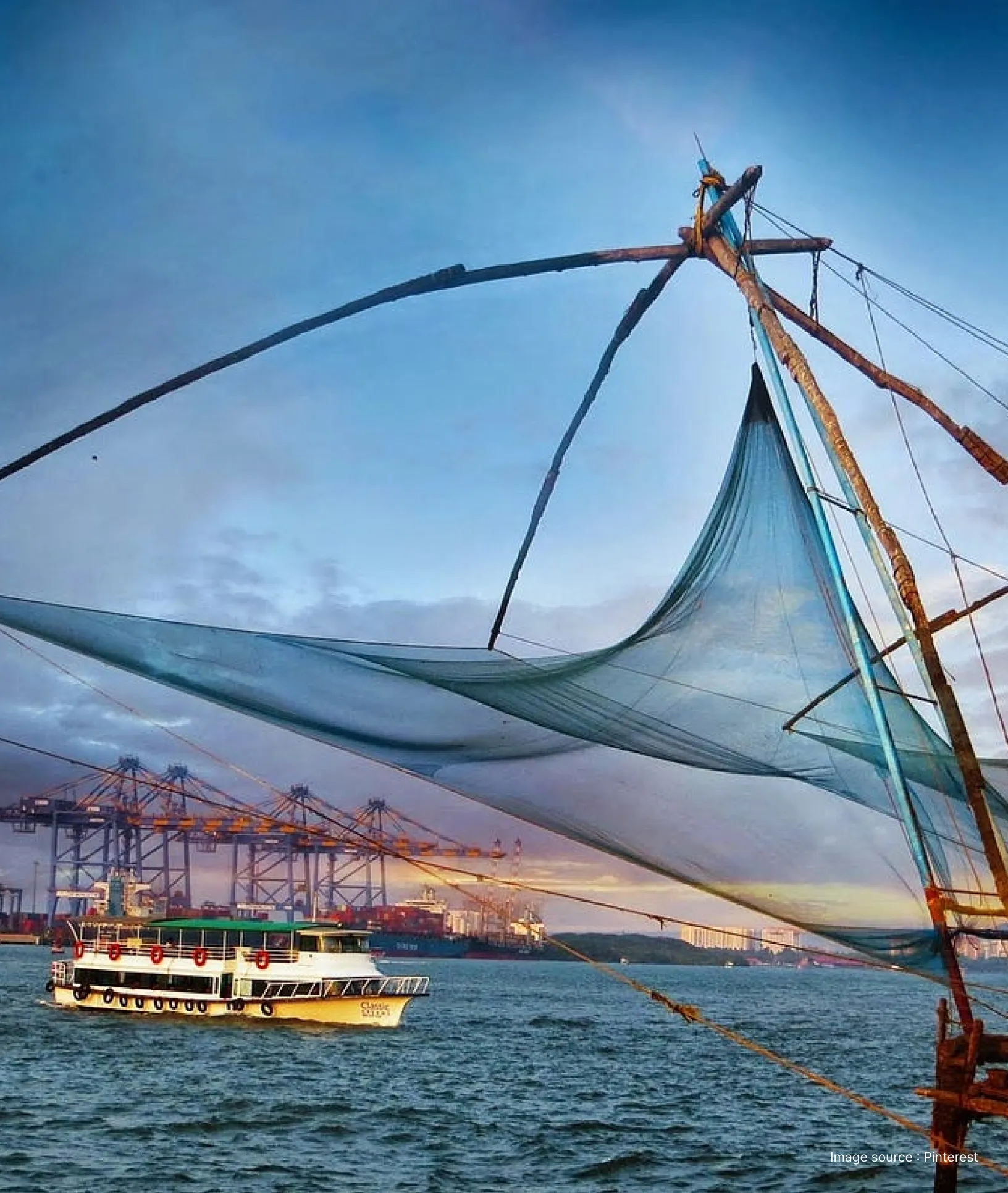 "Close-up of a Chinese fishing net in Fort Kochi with a tourist ferry and Vallarpadam terminal cranes in the background"