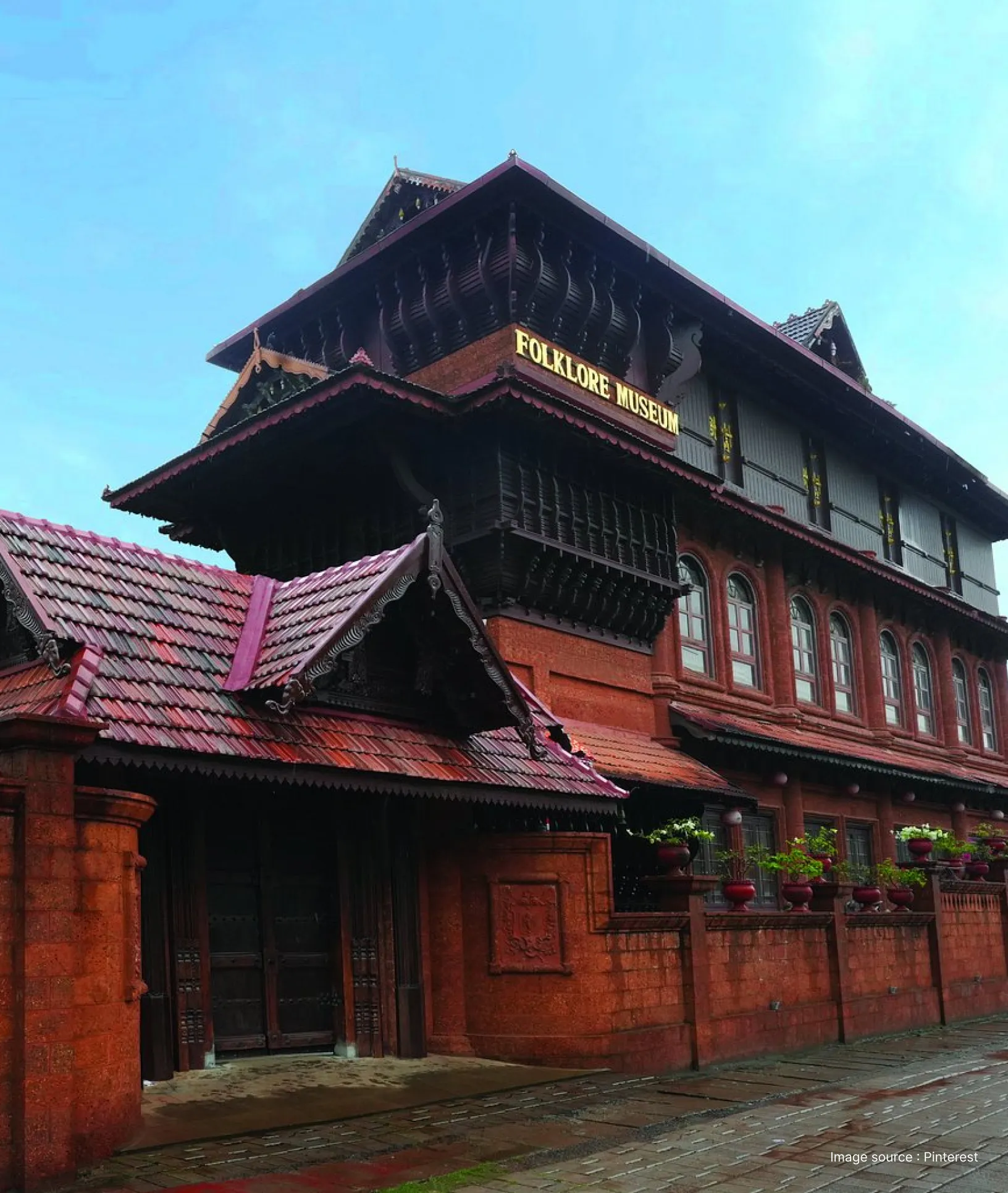 The ornate wooden facade and red laterite stone architecture of the Kerala Folklore Museum in Thevara, Kochi.