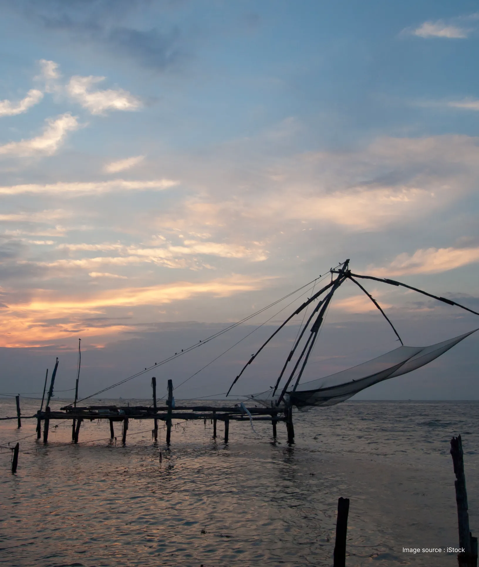 "Silhouette of a traditional Cheenavala Chinese fishing net at sunset on the Fort Kochi coastline.