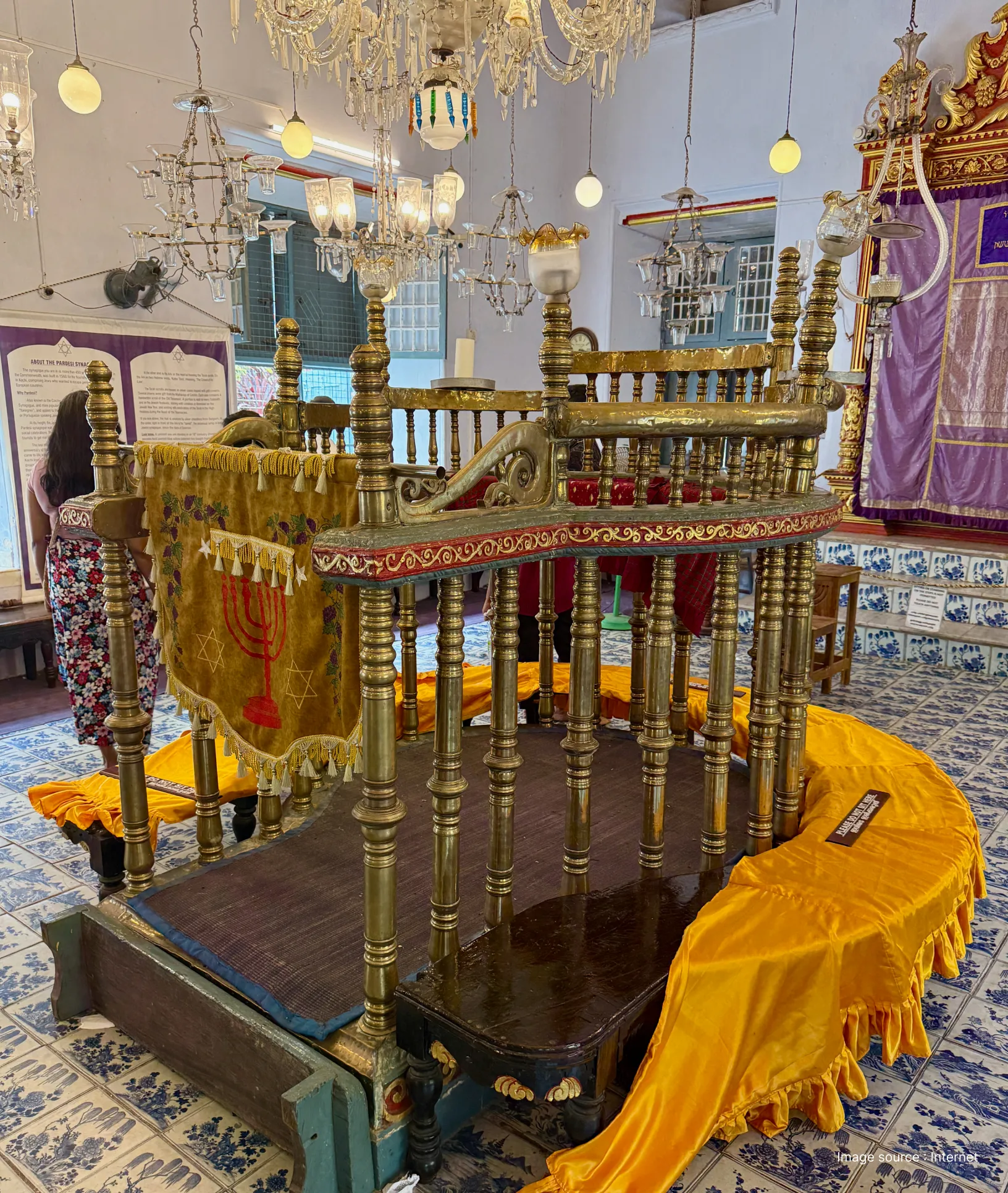 Interior of the Paradesi Synagogue in Mattancherry featuring the ornate brass pulpit, hand-painted blue willow floor tiles, and glass chandeliers.