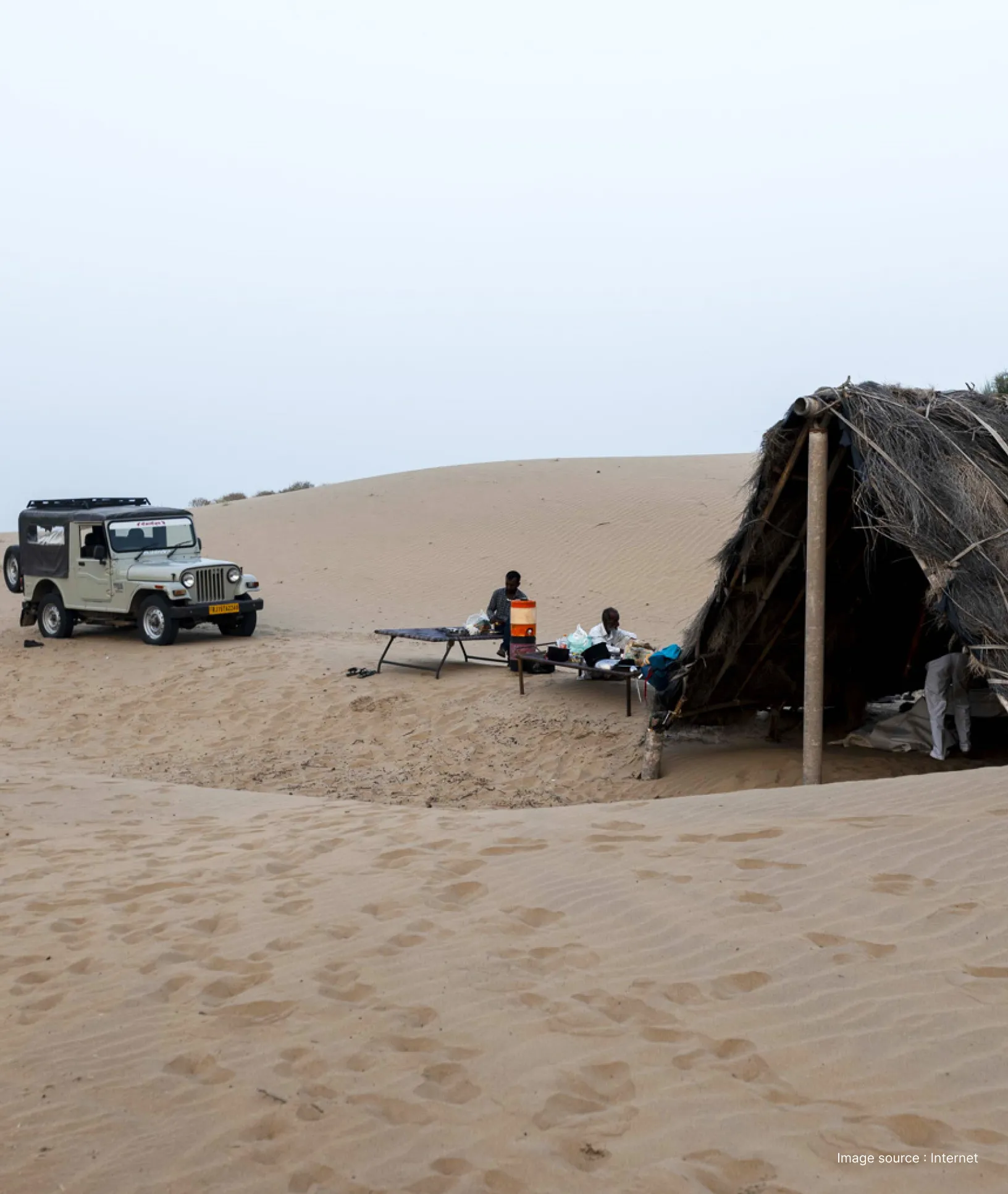 a temporary camp set up in the dunes of jaisalmer desert with black tent and a white safari jeep in view