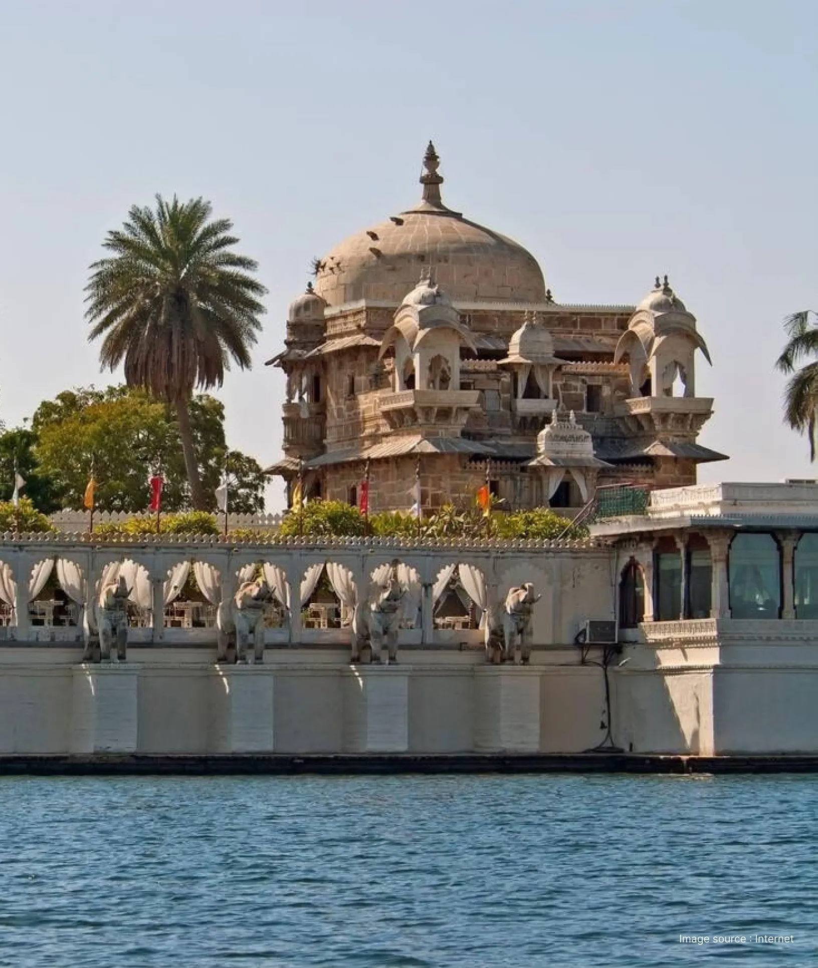 lakeside view of the intricate architecture of the jag mandir palace with one palm tree