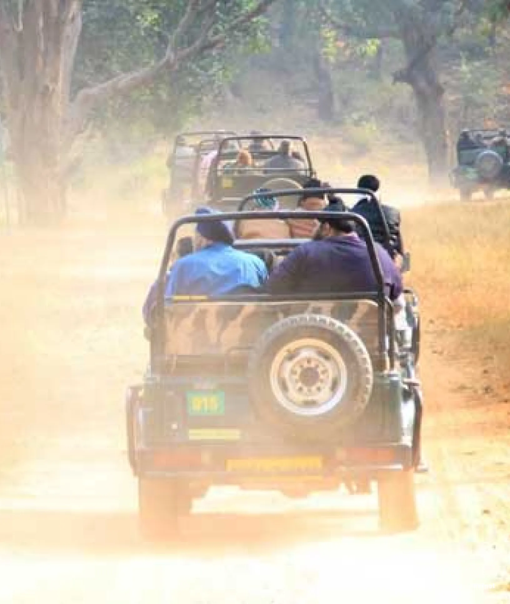 two jeeps with safari tourists drive ahead on a dry road