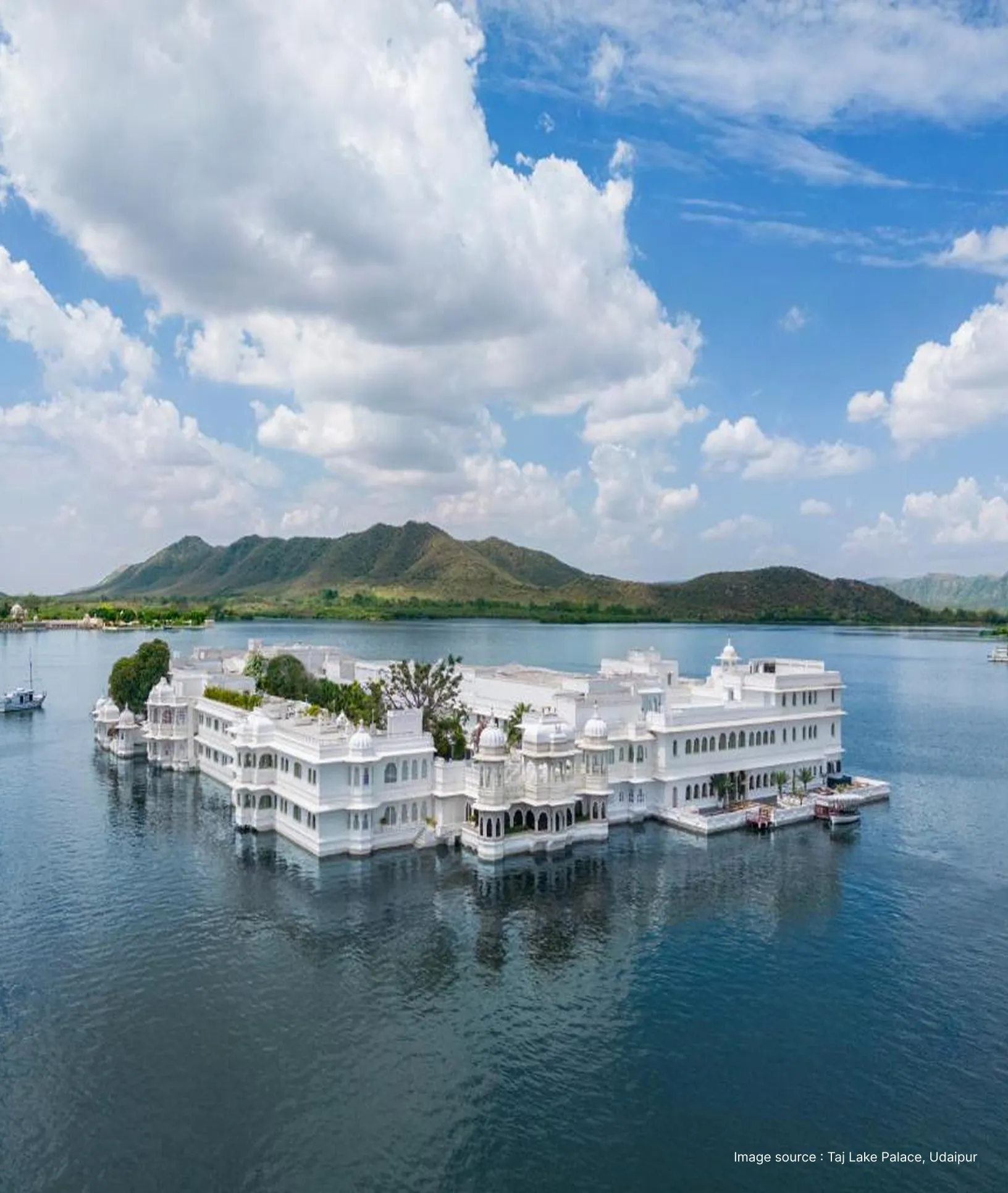 an aerial shot of the ethereal taj lake palace, floating in the middle of lake pichola with green hills in the backdrop