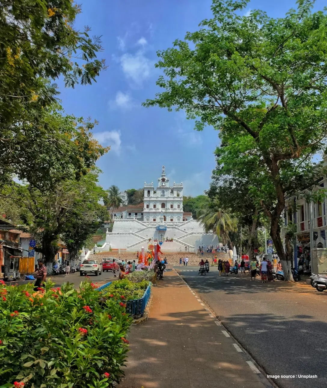 a church in goa surrounded by green trees and colorful flowers on a clear day