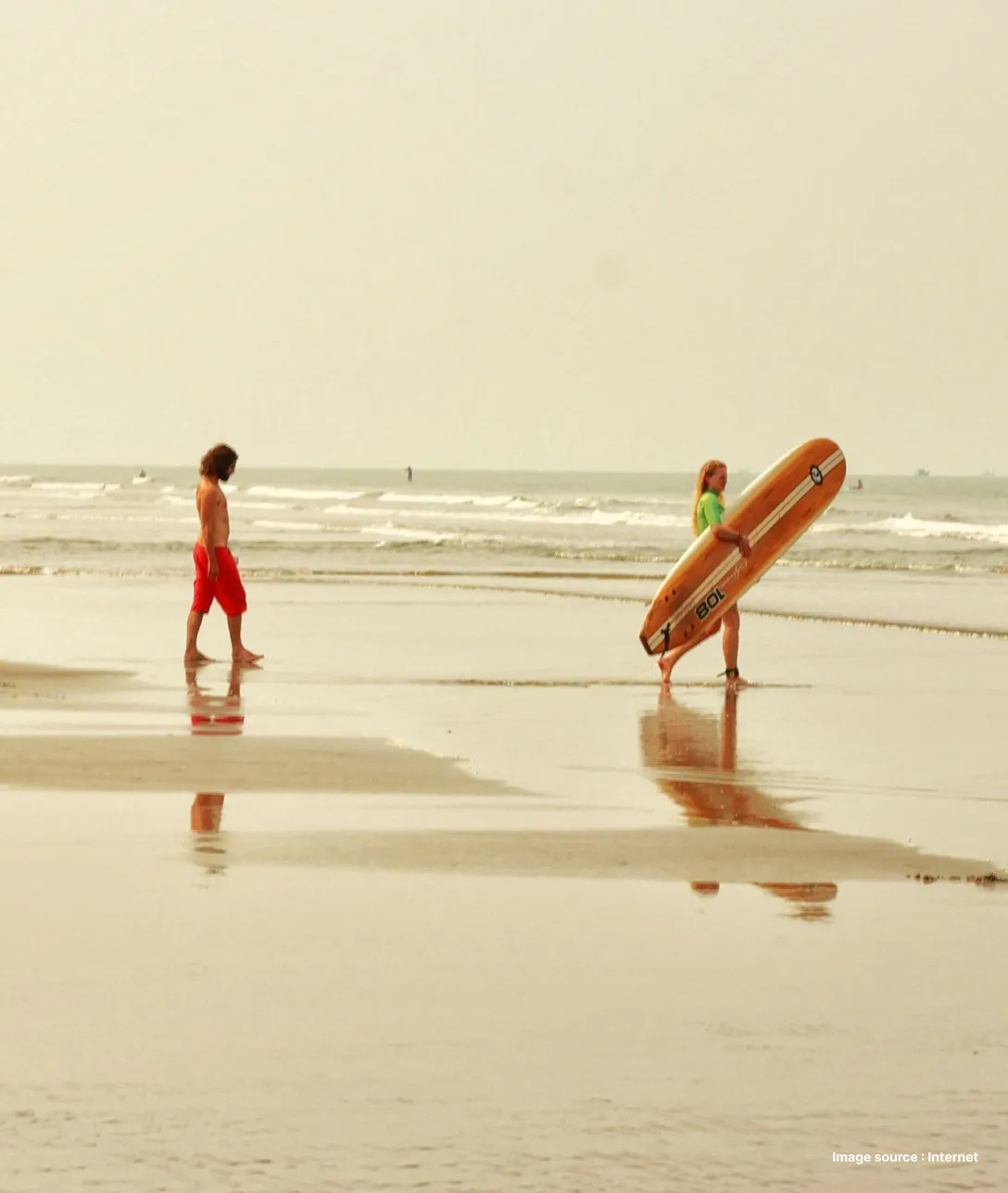 tourists walking on a beach at dusk, one carrying a surf board