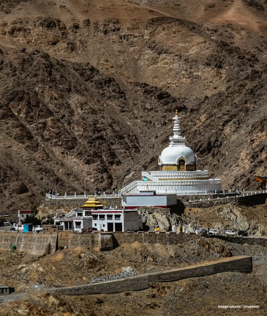 a distant shot of the shanti stupa's white dome shaped structure against mountains