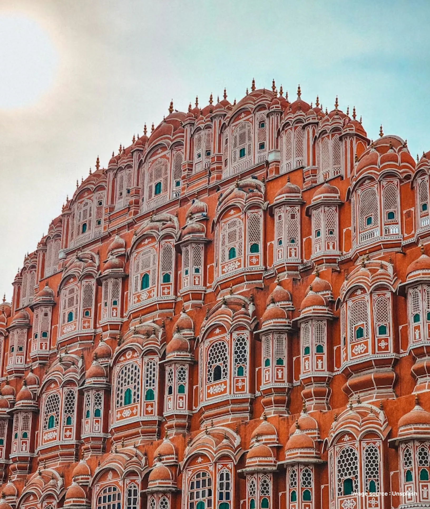 a side angled shot of jaipur's iconic hawal mahal's pink facade with the sun in frame