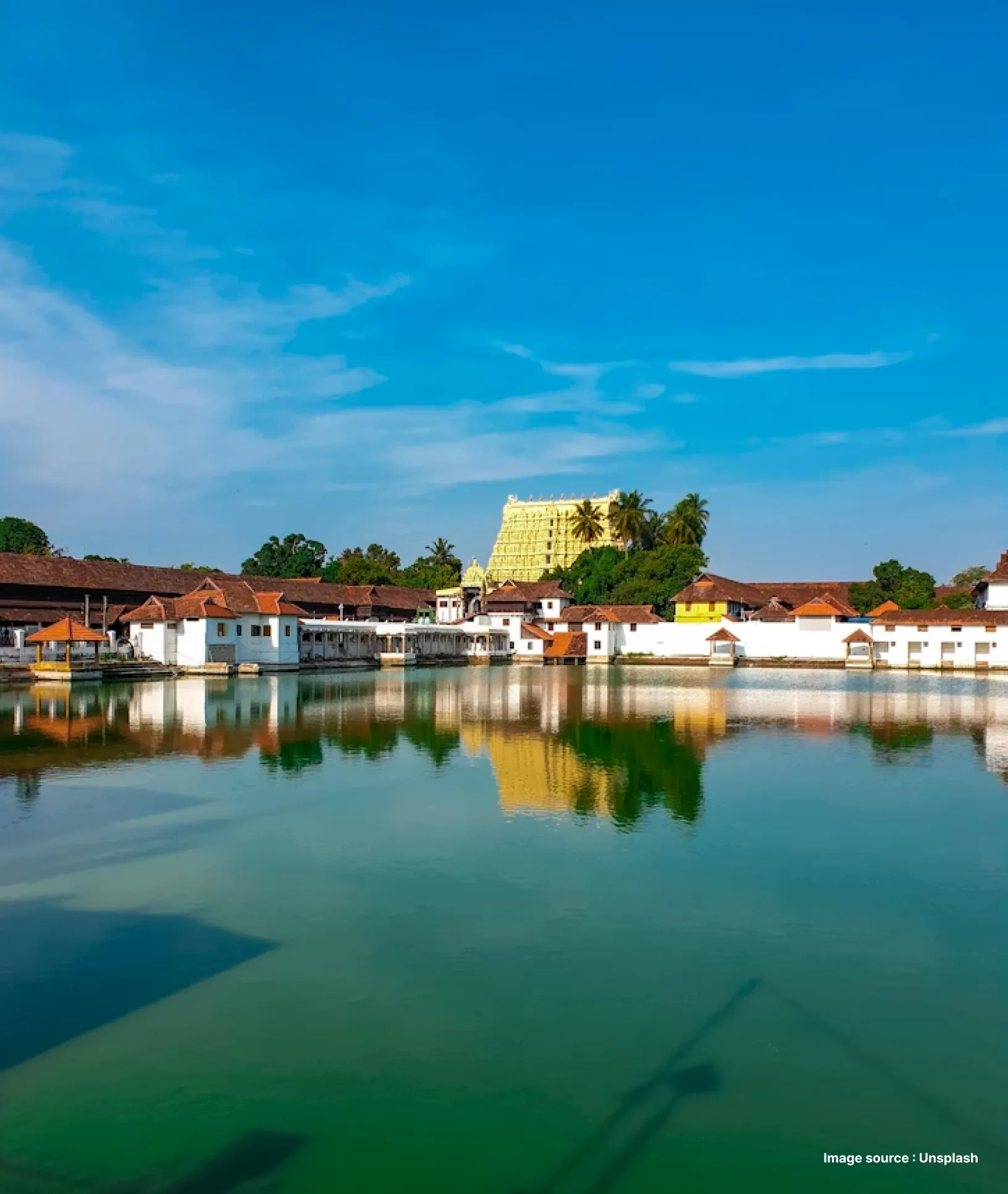 a distant shot of the golden building of sree padmanabhaswamy temple in trivandrum with a pond