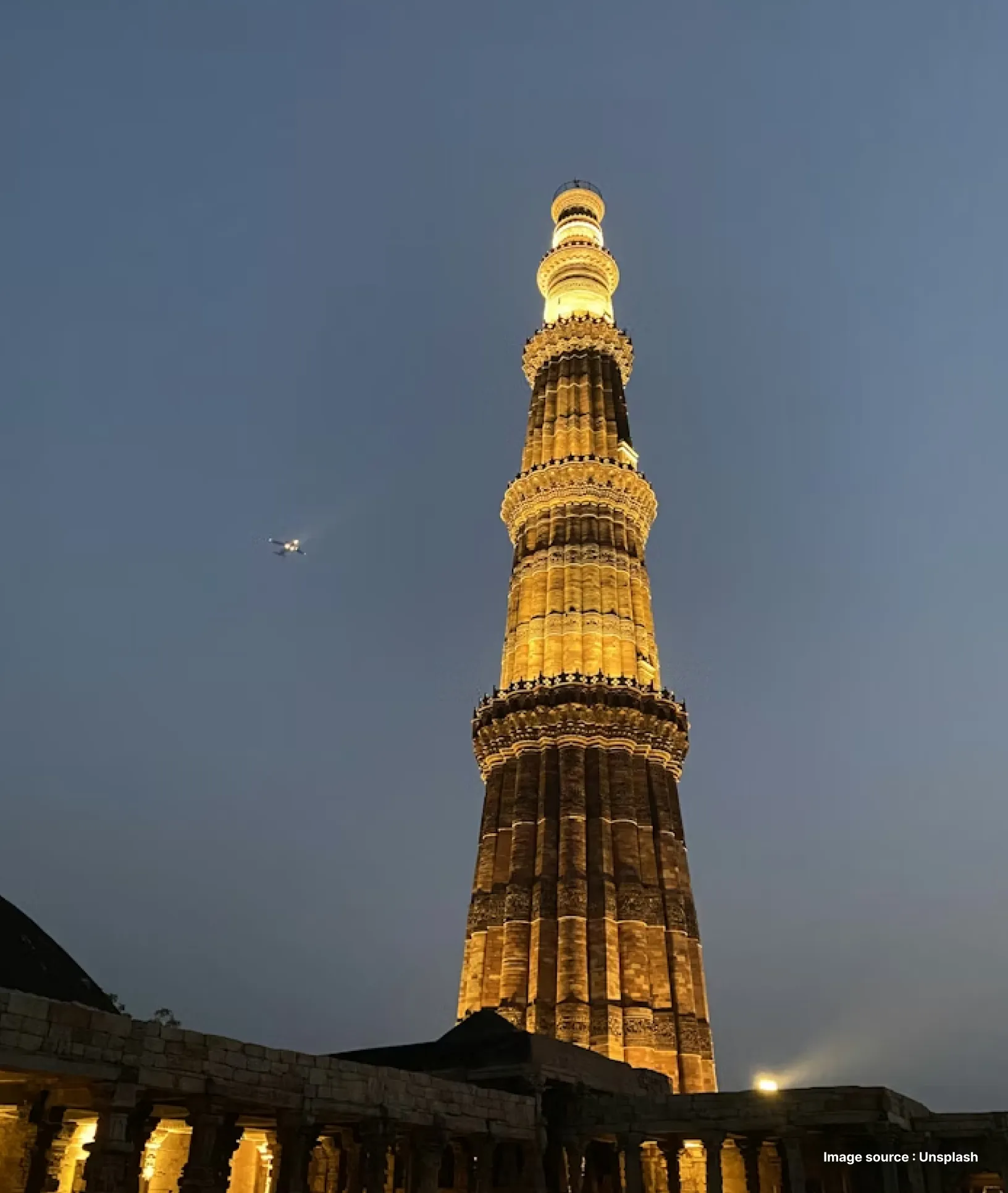 nightview of delhi's ancient qutub minar, lit up with golden lights