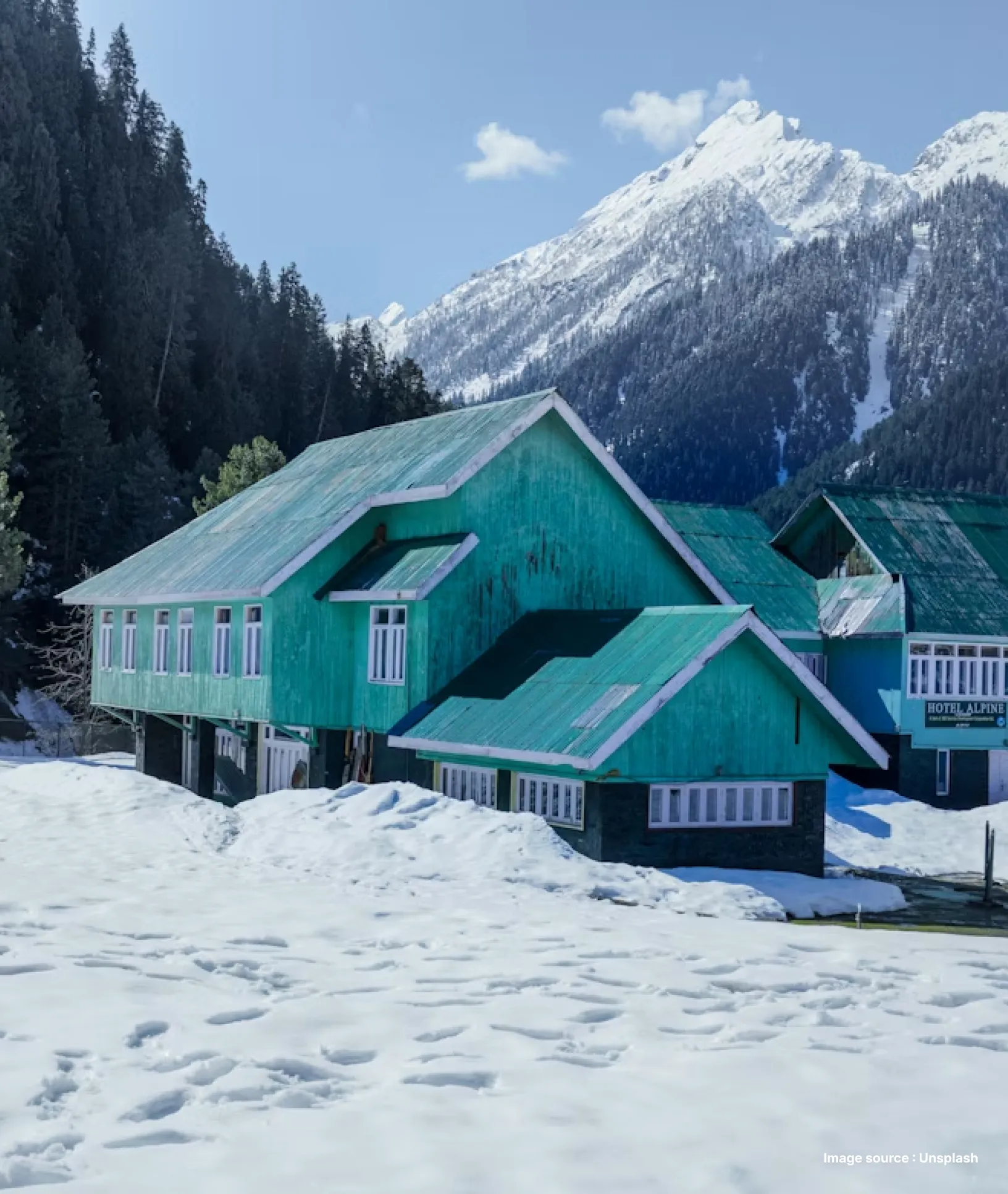 a blue wooden cottage in a snow covered valley with pine trees in the back