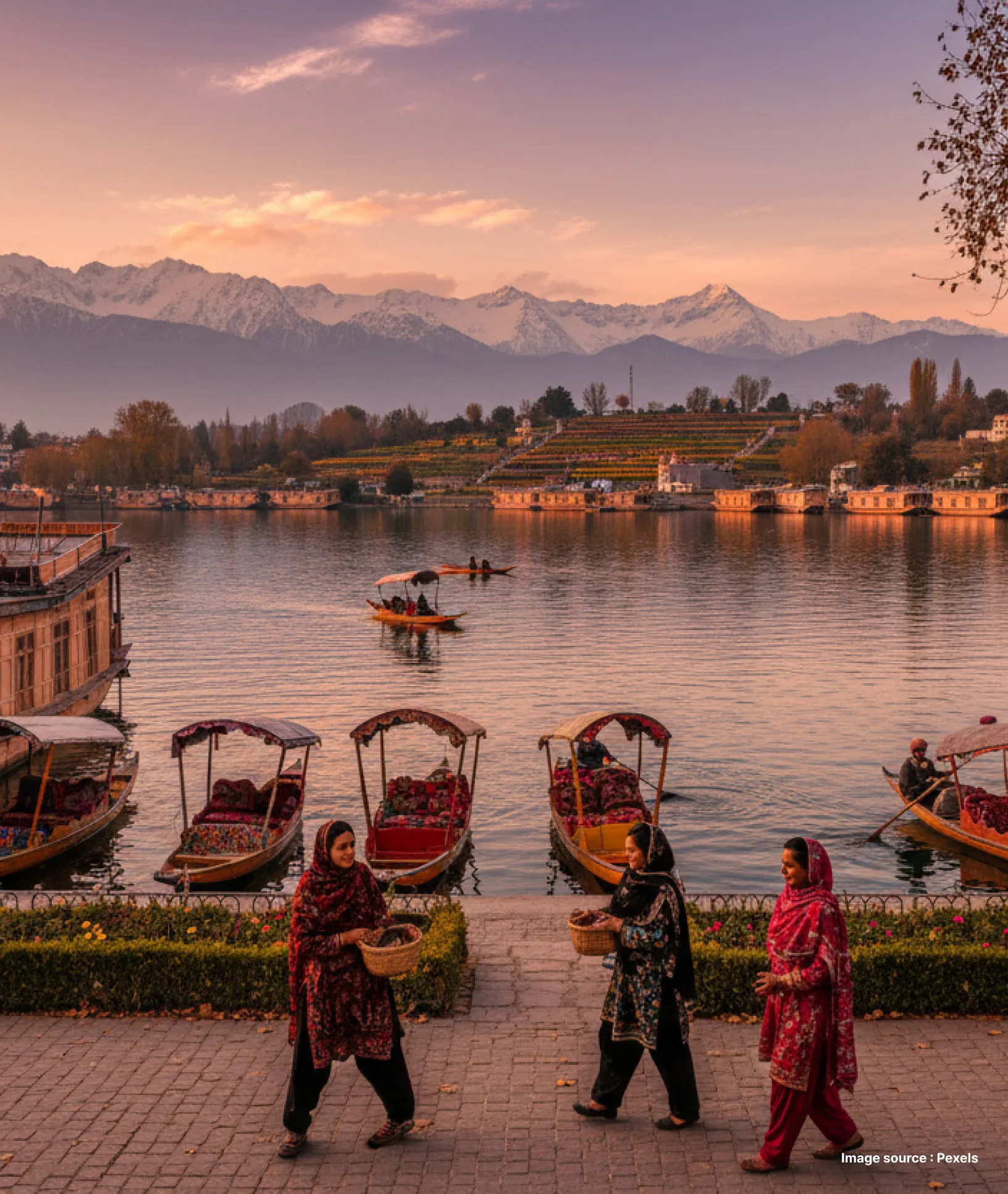 tourists walk past the dal lake, where three shikaras are parked at sunset