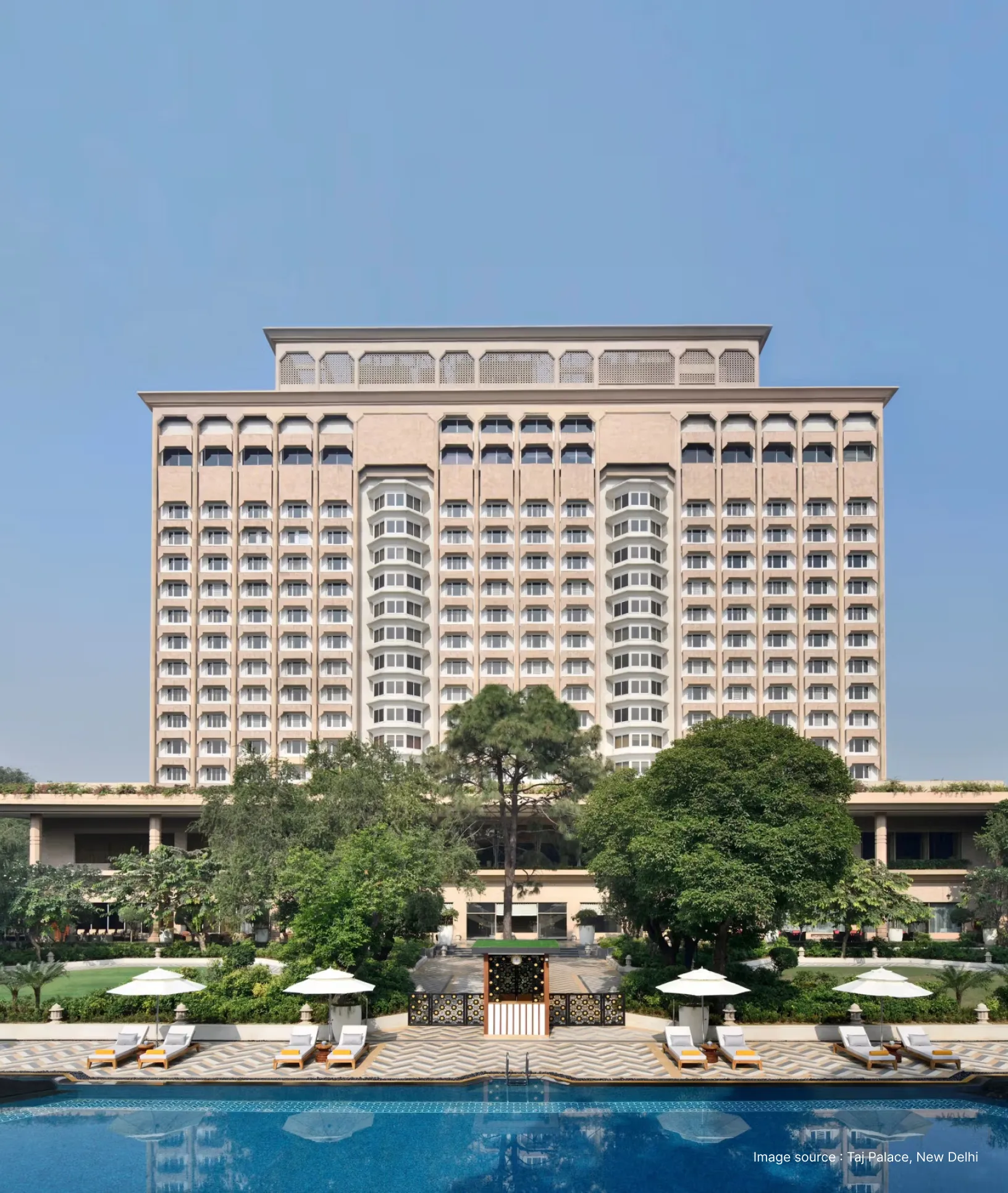 distant view of the tall taj palace building in new delhi with trees and pool in view