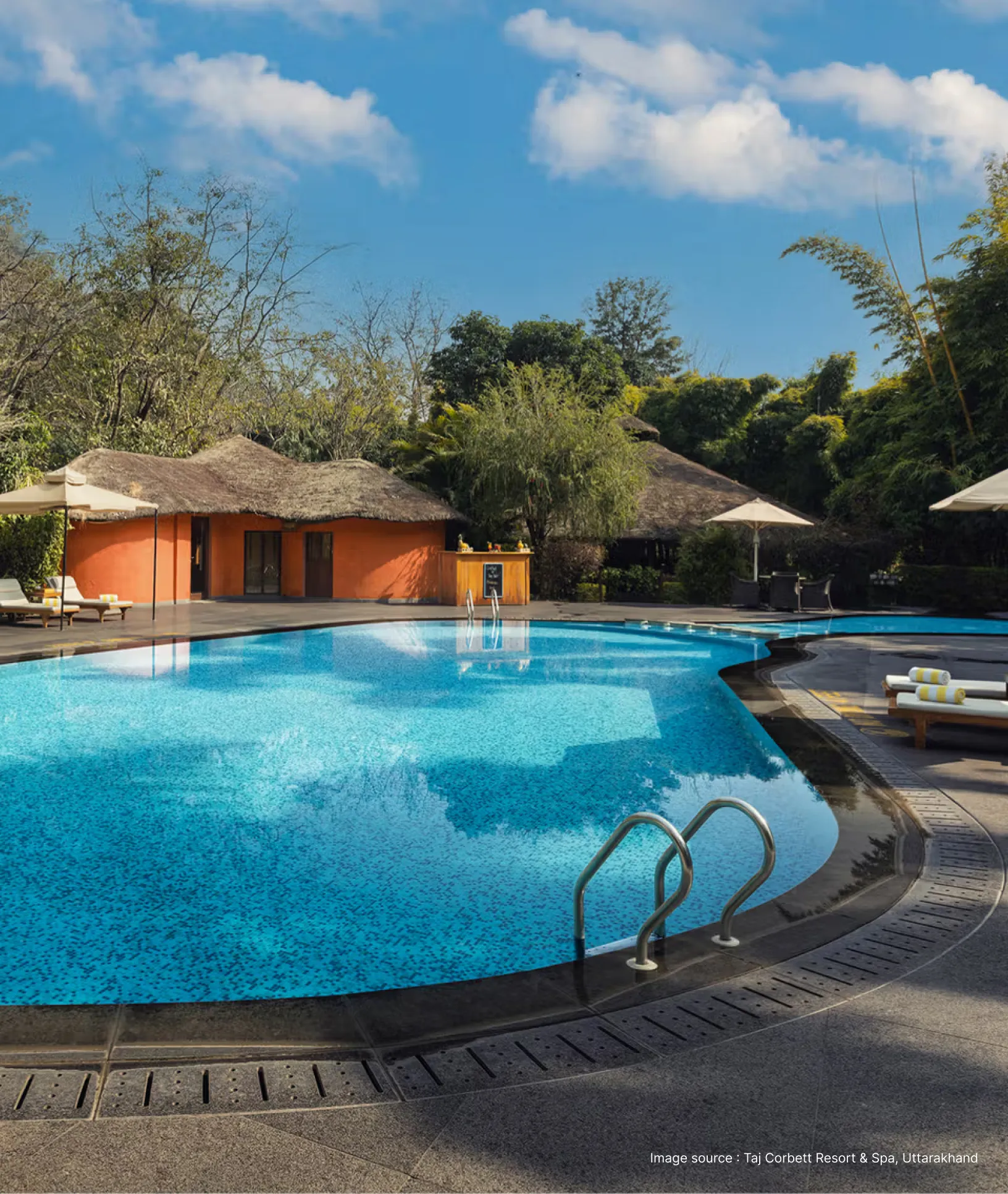 pool side view of the taj corbett resort with a orange shelter and trees in the background