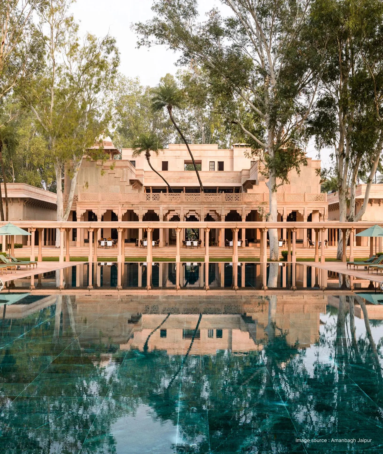 pool view of the amanbagh resort with archways in halls and trees over the pool