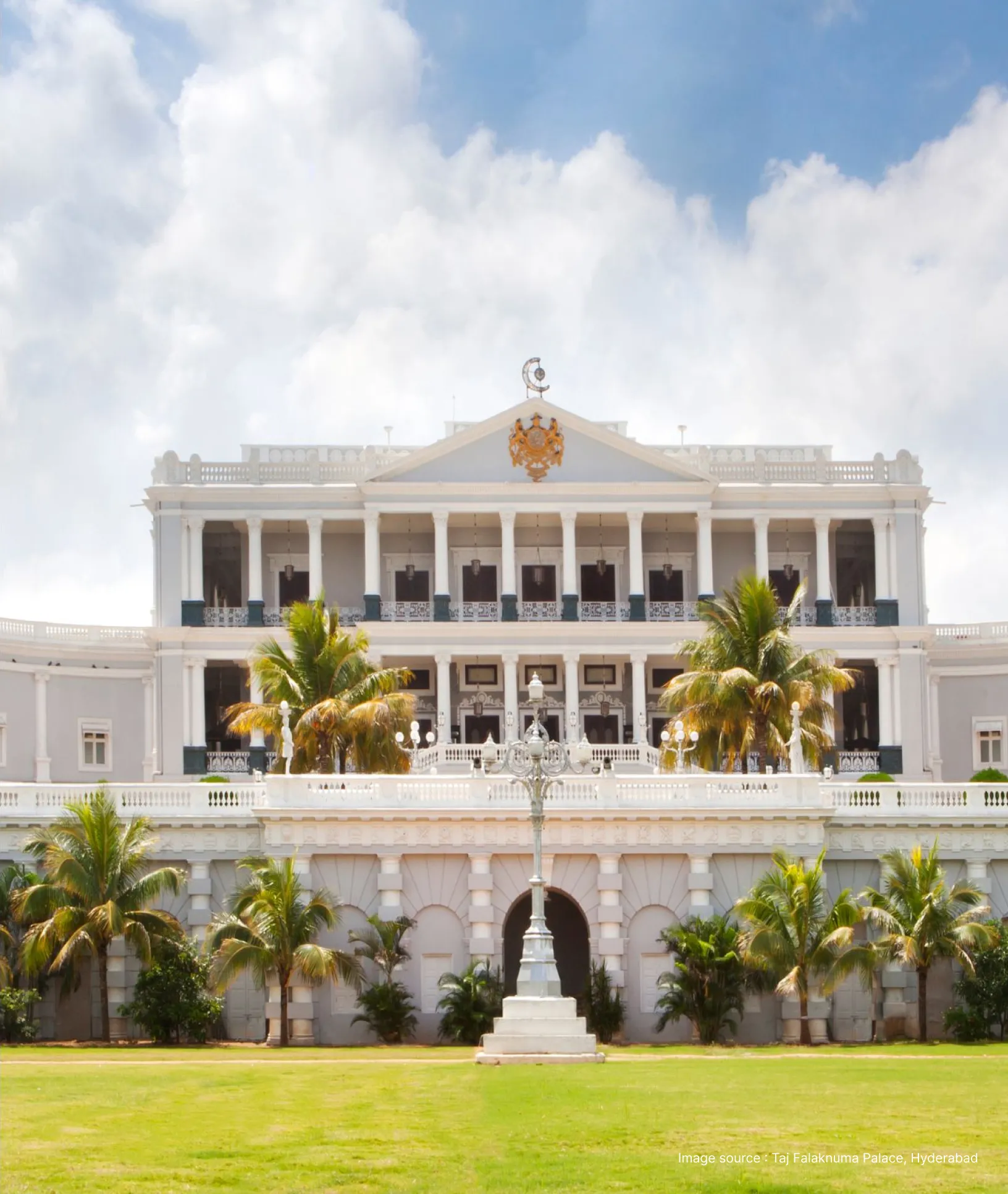 front view of the white building of the taj falaknuma palace with palm trees