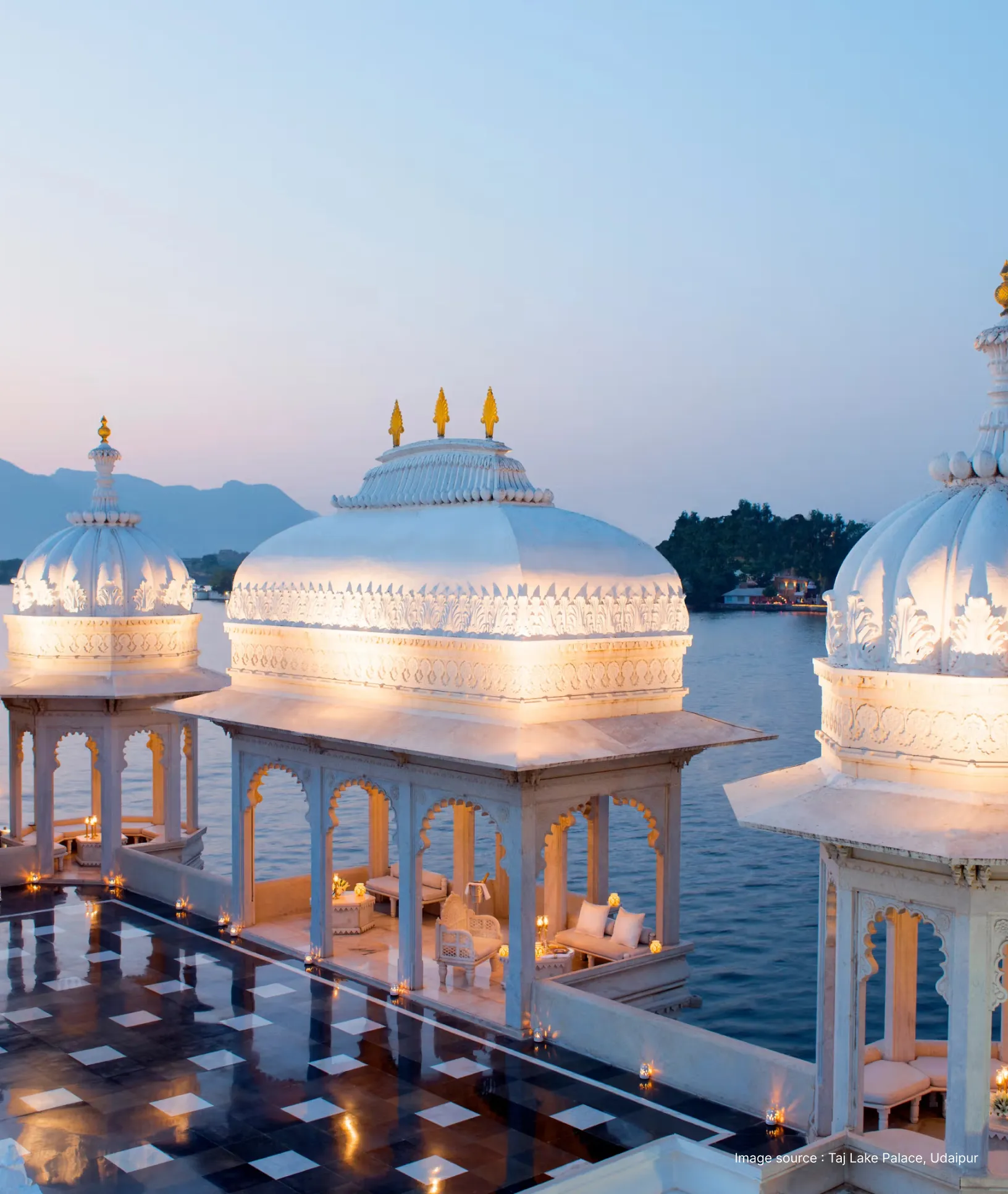 lit up white domes of the taj lake palace at sunset
