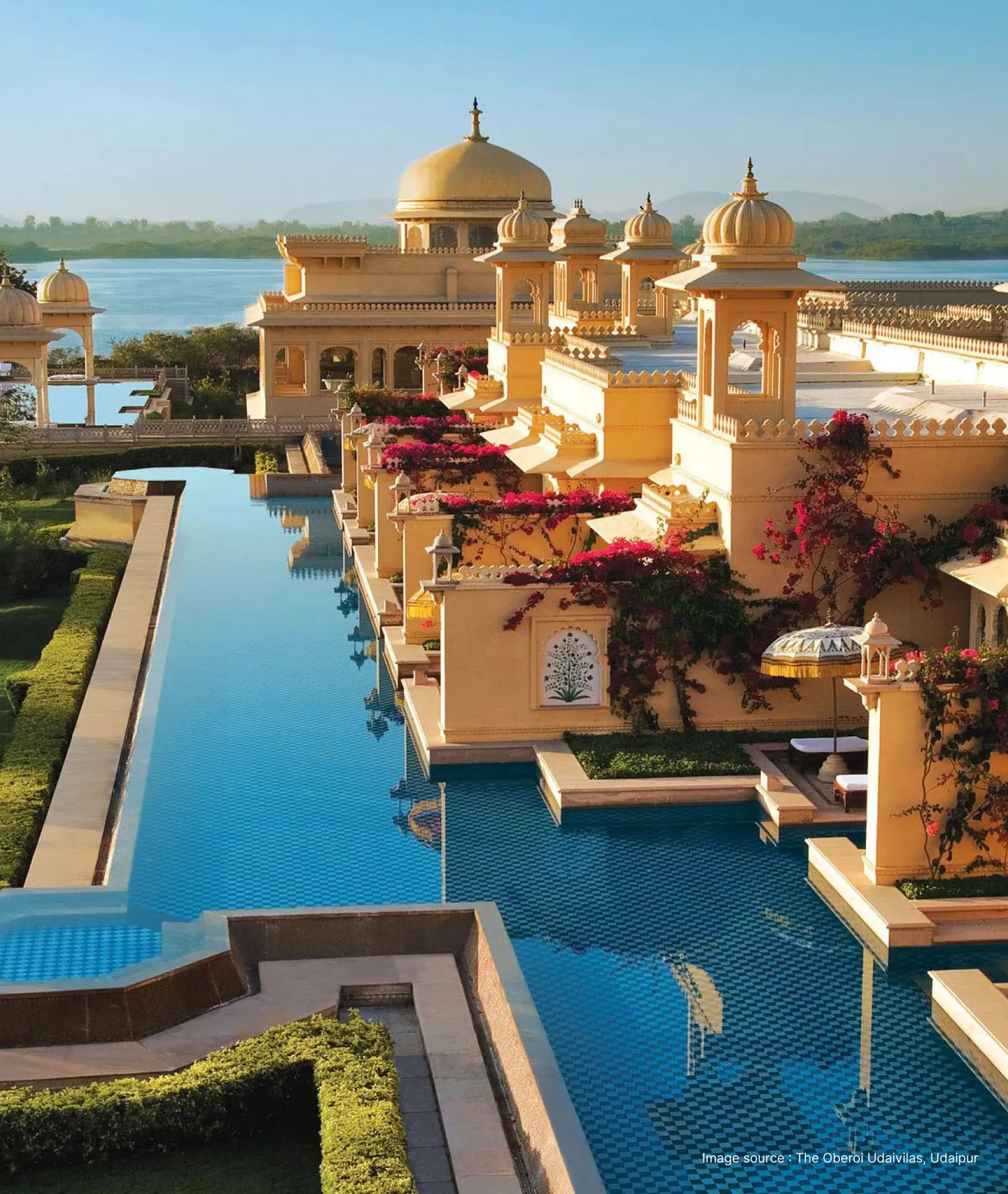 poolside view of the oberoi udaivilas with lake pichola in a distance and its grand yellow domes