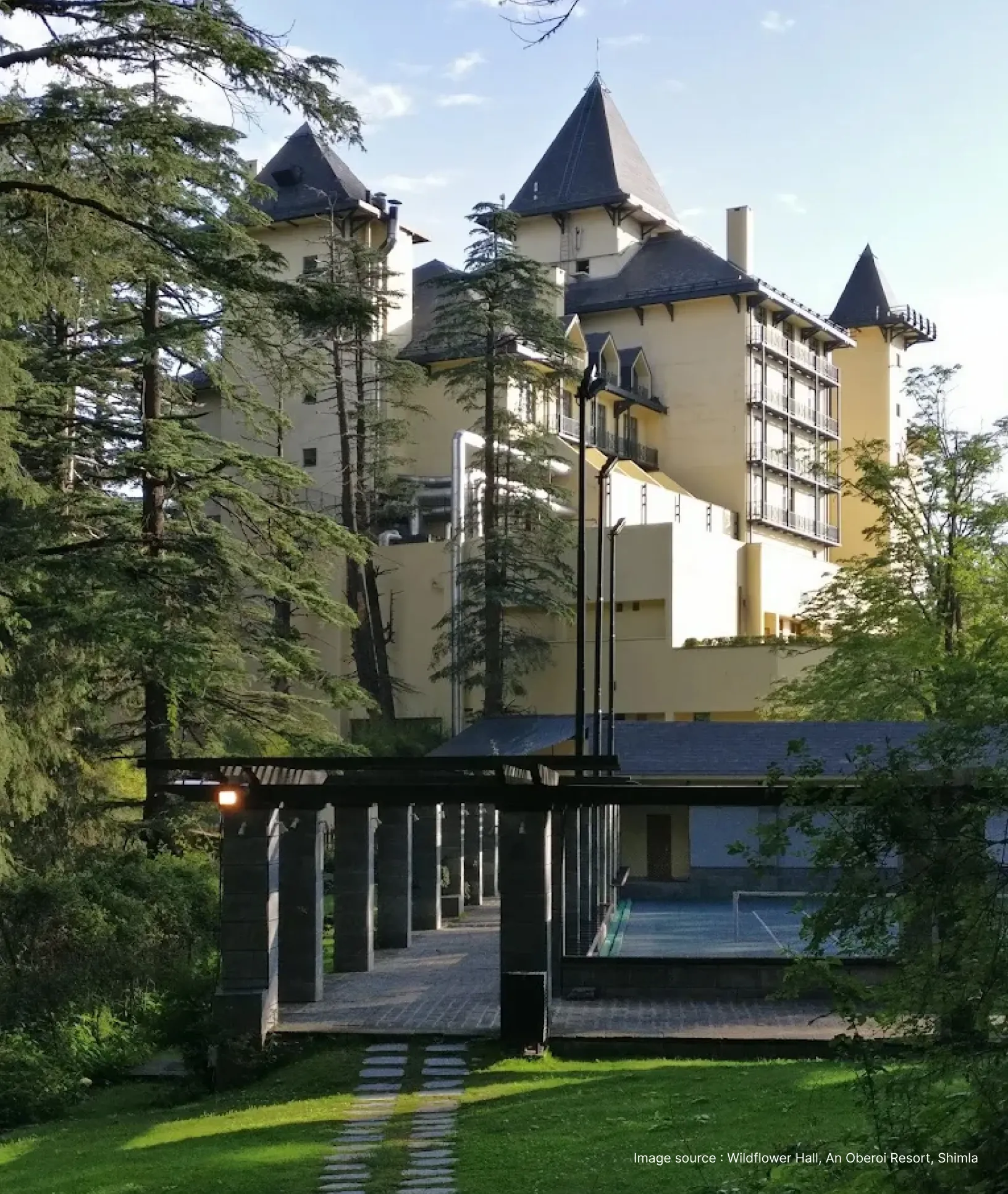 side angled view of the wildflower hall resort in shimla with tall trees in sunlight