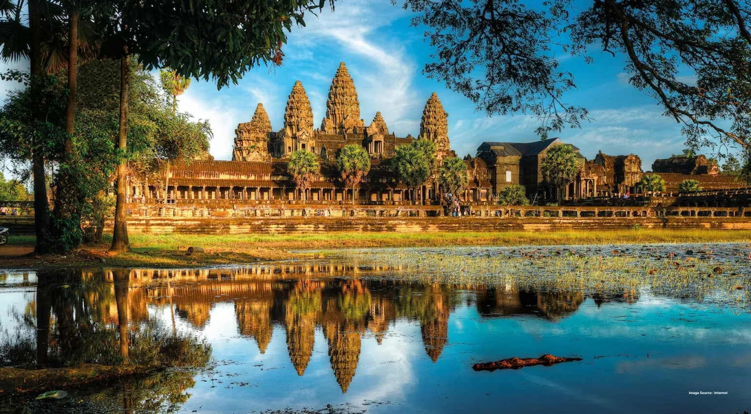 a gorgeous daytime view of angkor wat ancient temples across a lake and trees