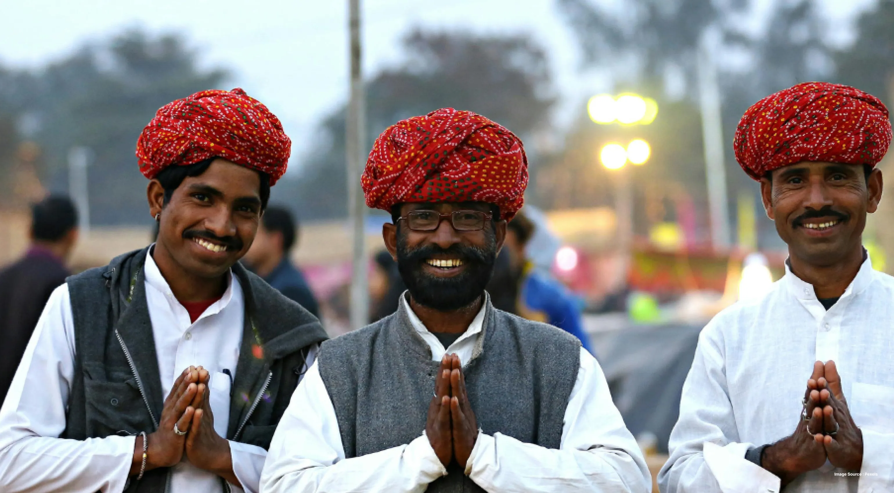 three indian men in red turbans smiling as they do namaste hand gesture with their palms together