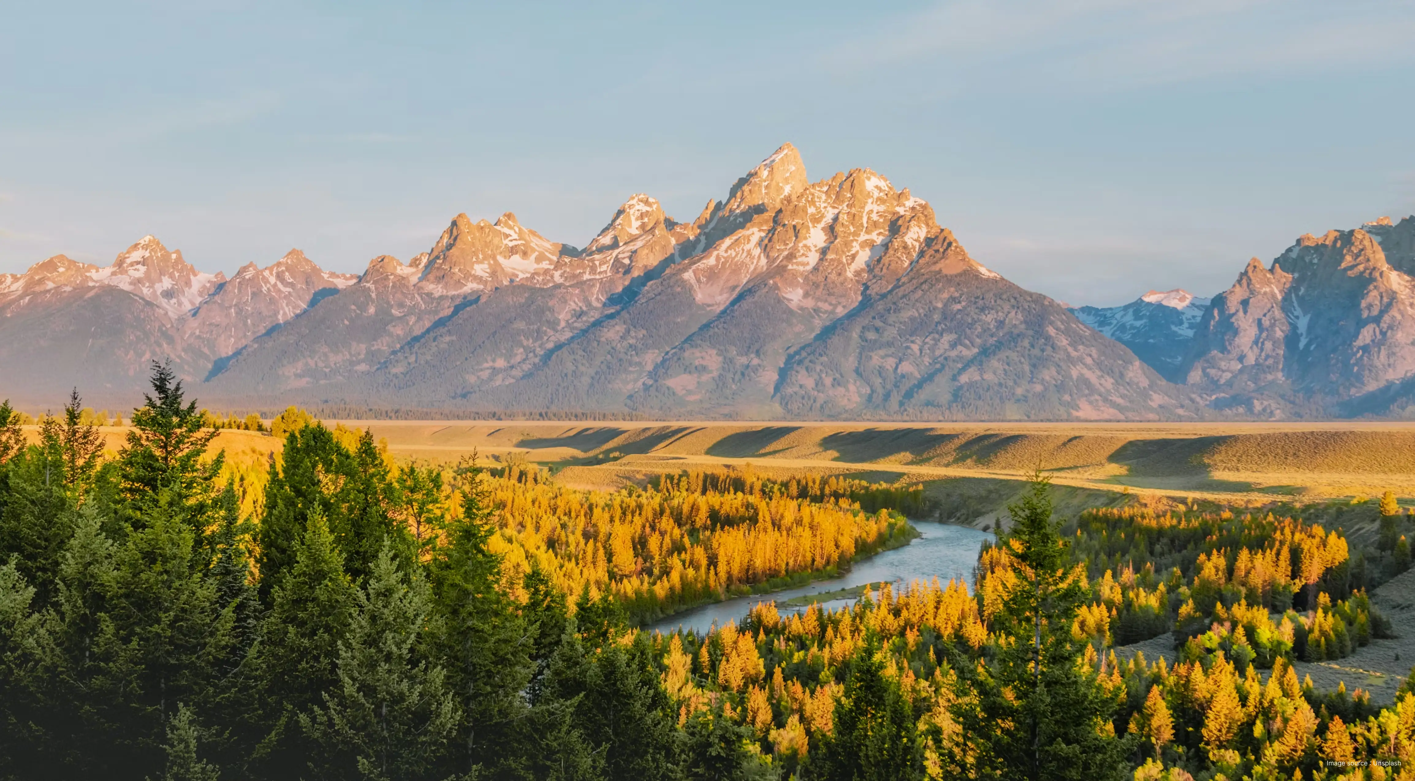 sunrise over rugged mountain peaks surrounded by lush green plains and a river