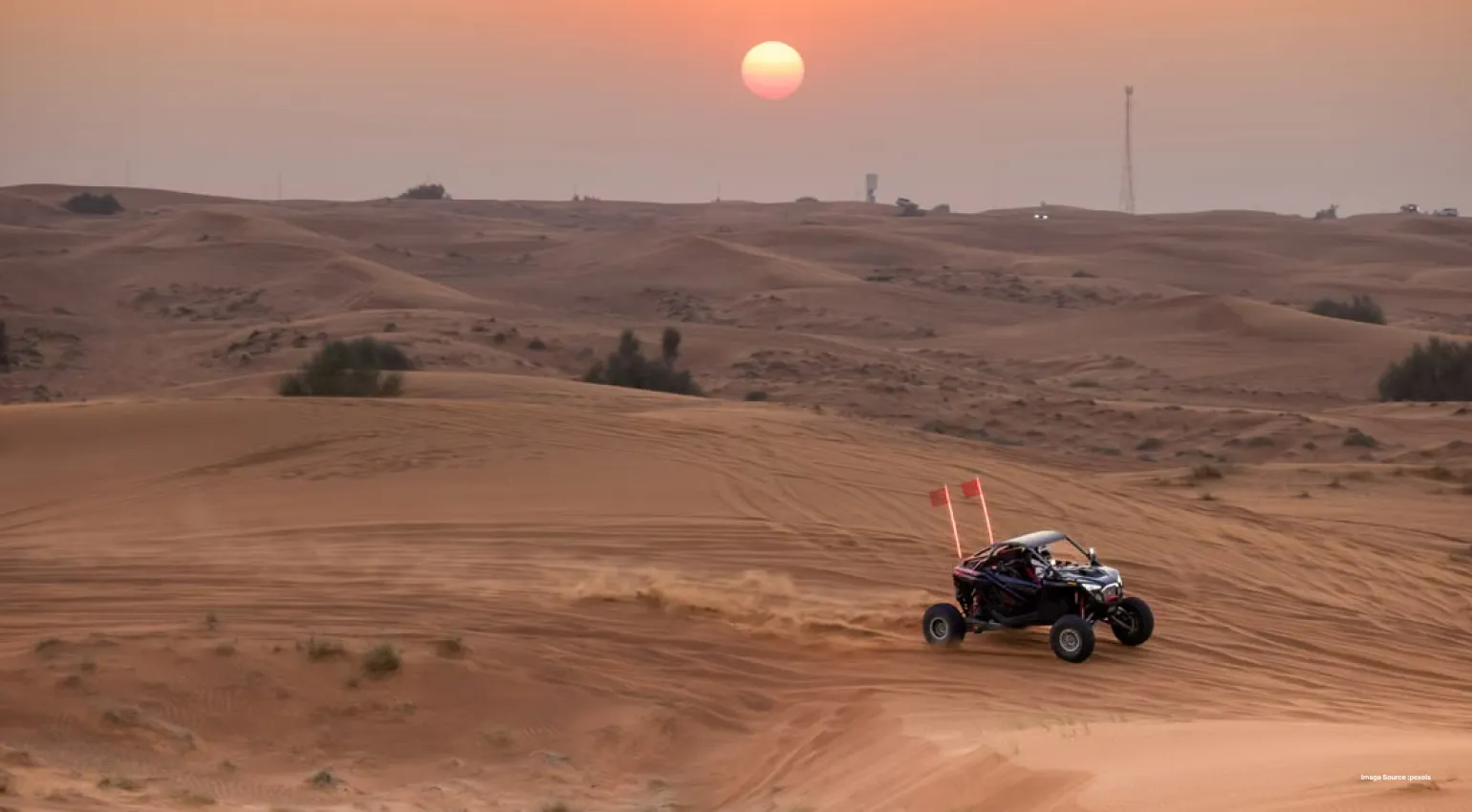 Off-road dune buggy driving across desert sand dunes at sunset.