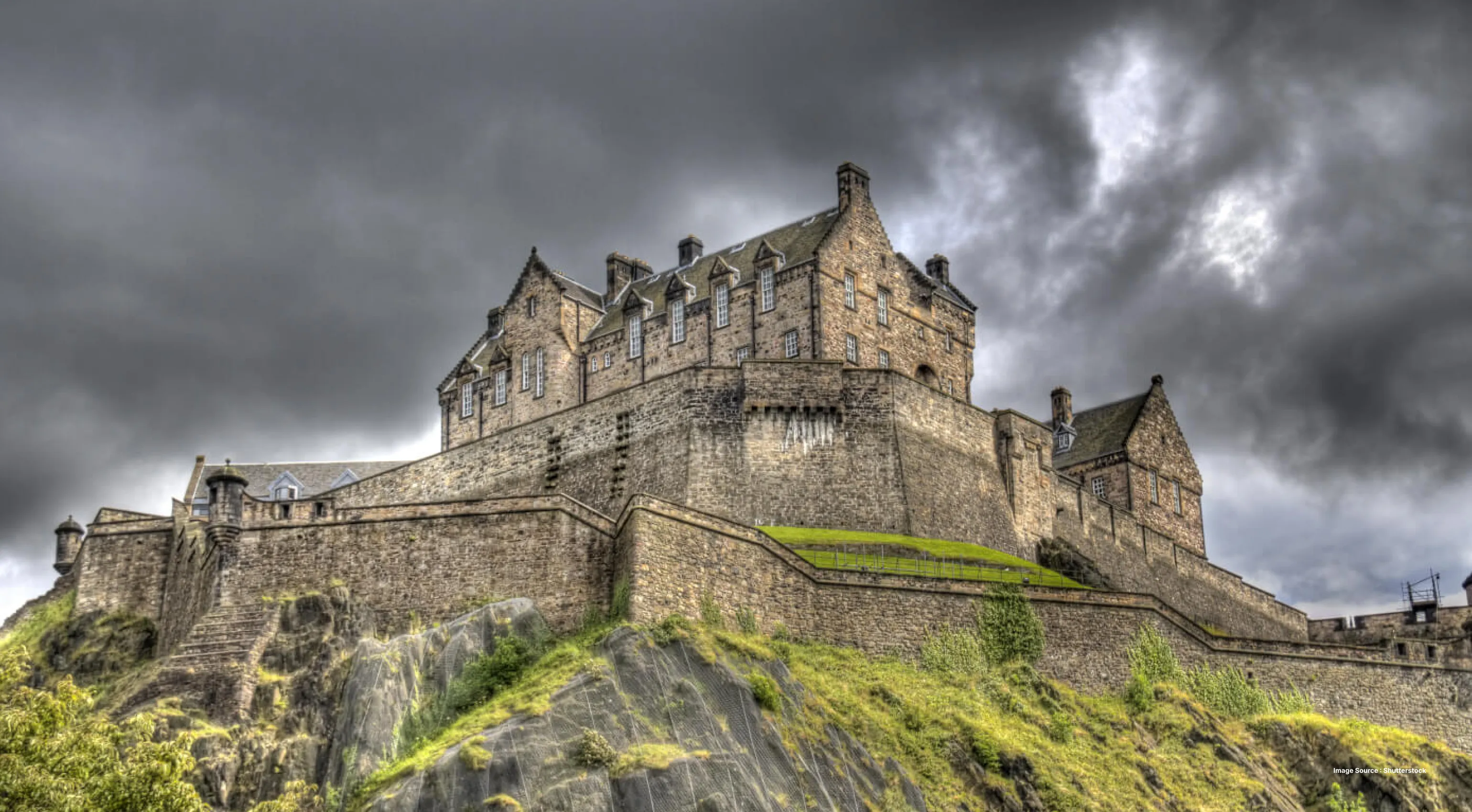 a mystical looking ancient castle on a green hilltop with a dark cloudy sky