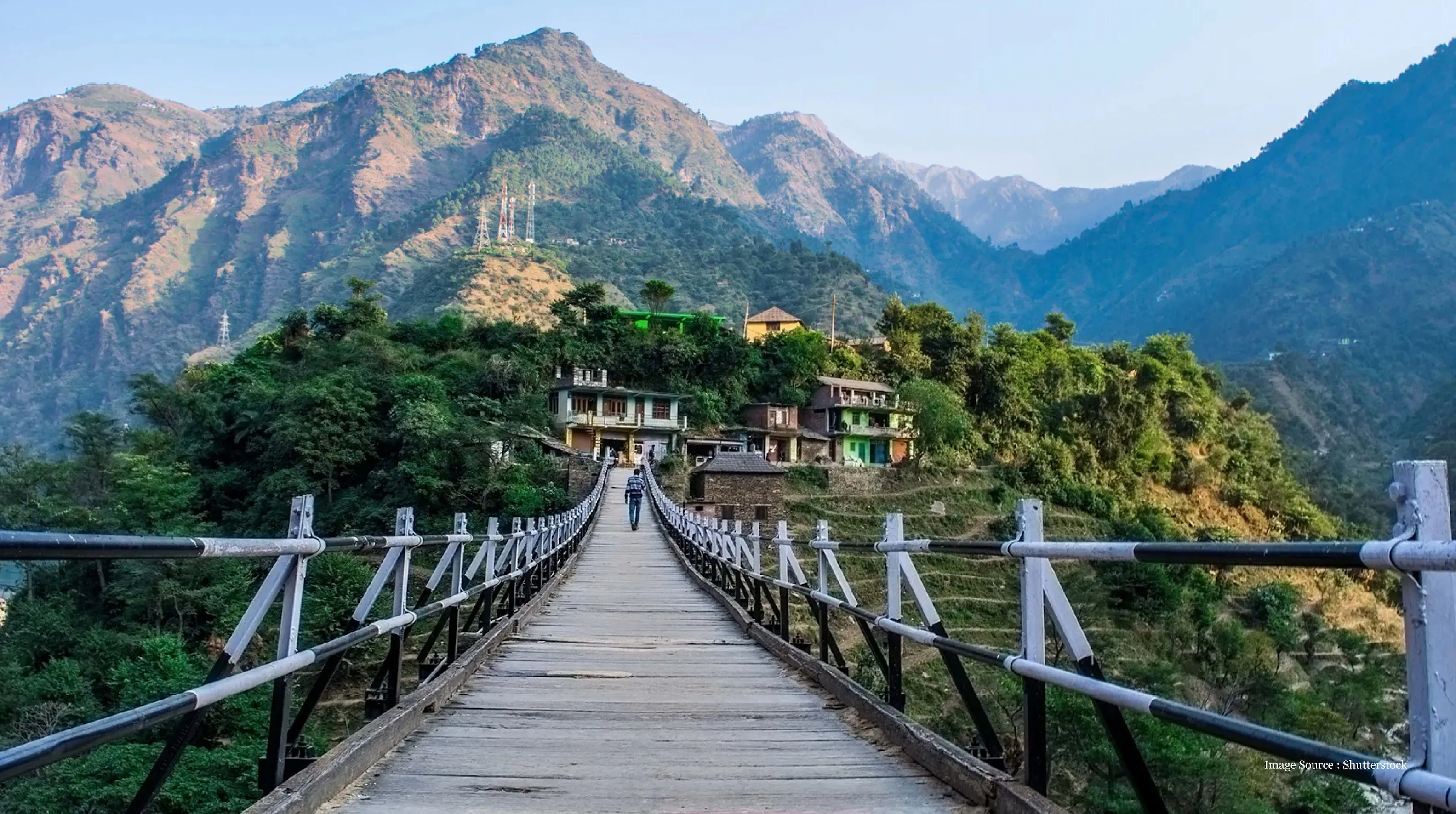 Snow-capped mountains, lush greenery, a wooden bridge, and scenic village houses in Himachal Pradesh, India