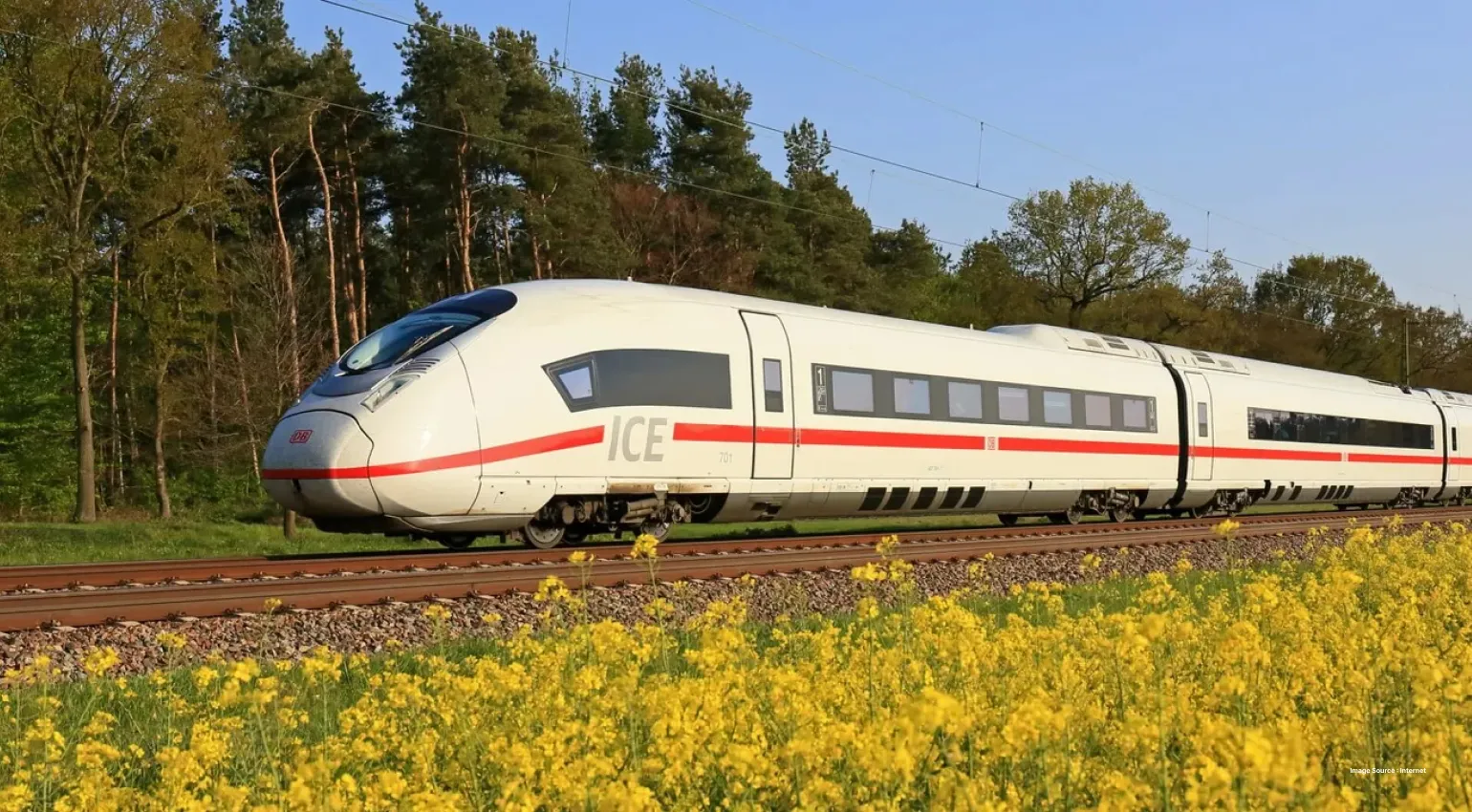 a white ICE train standing on a railway track in middle of a beautiful yellow field and trees