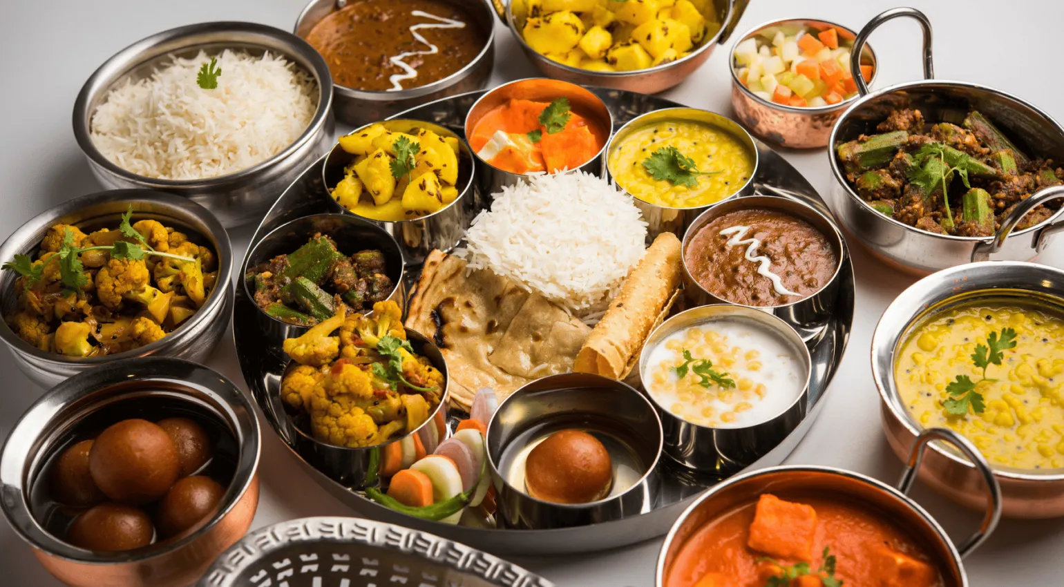 a relishing platter of north indian food with multiple curries, rice, desserts and other colorful dishes