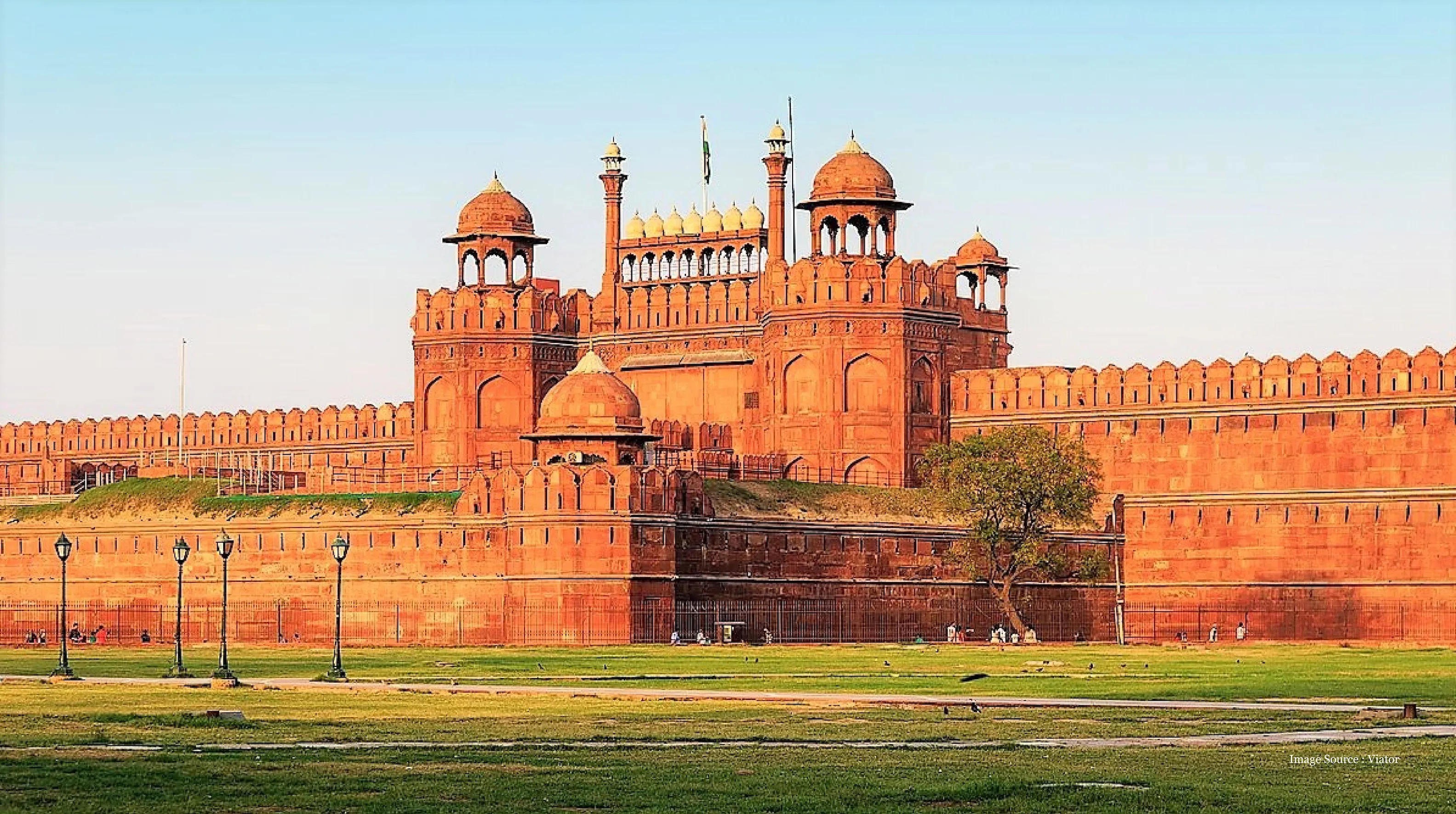 Luxury Golden Triangle Agra tour featuring the magnificent Red Fort in Delhi, with its grand Mughal architecture and expansive lush green lawns under a clear sky