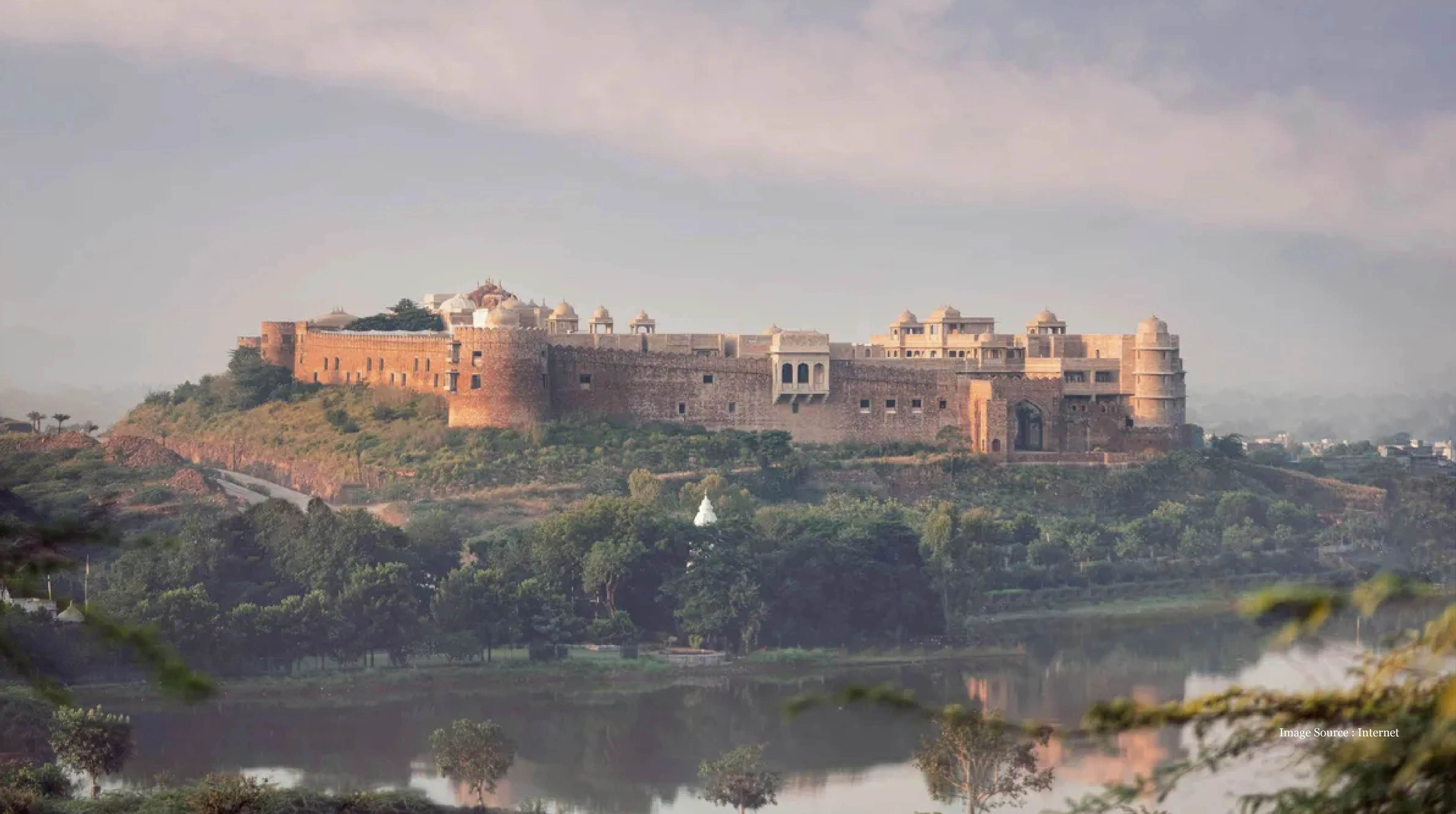 Rajasthan luxury spa at Six Senses Fort Barwara, showcasing a majestic fort on a hilltop surrounded by lush greenery and a tranquil lakeside setting