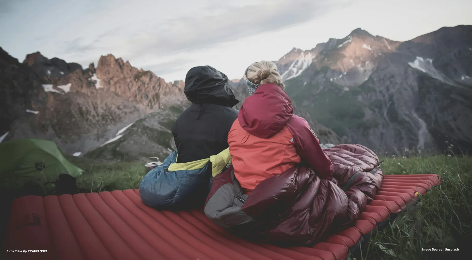 2 people sitting on sleeping pads looking over at the mountains