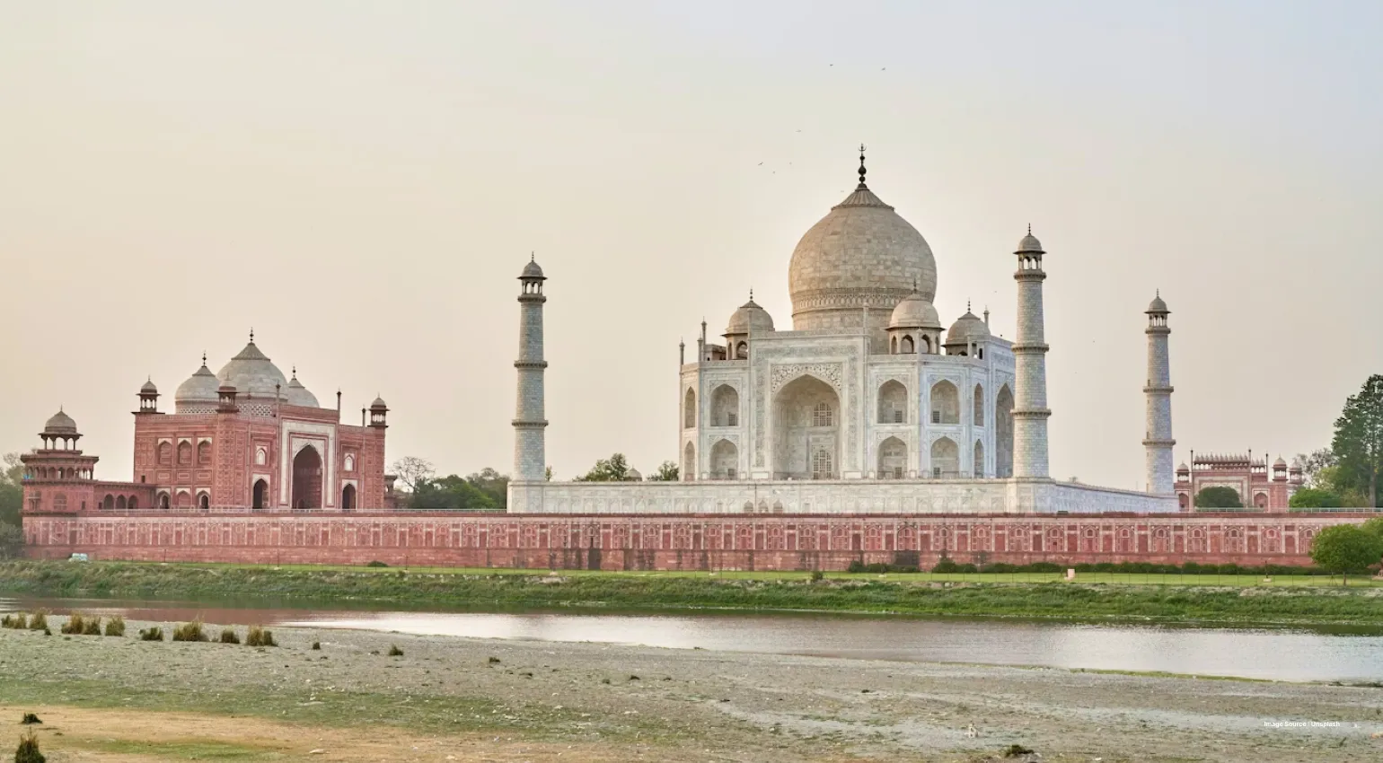 A side view of the taj mahal and its red sandstone gate from a distance at sunset