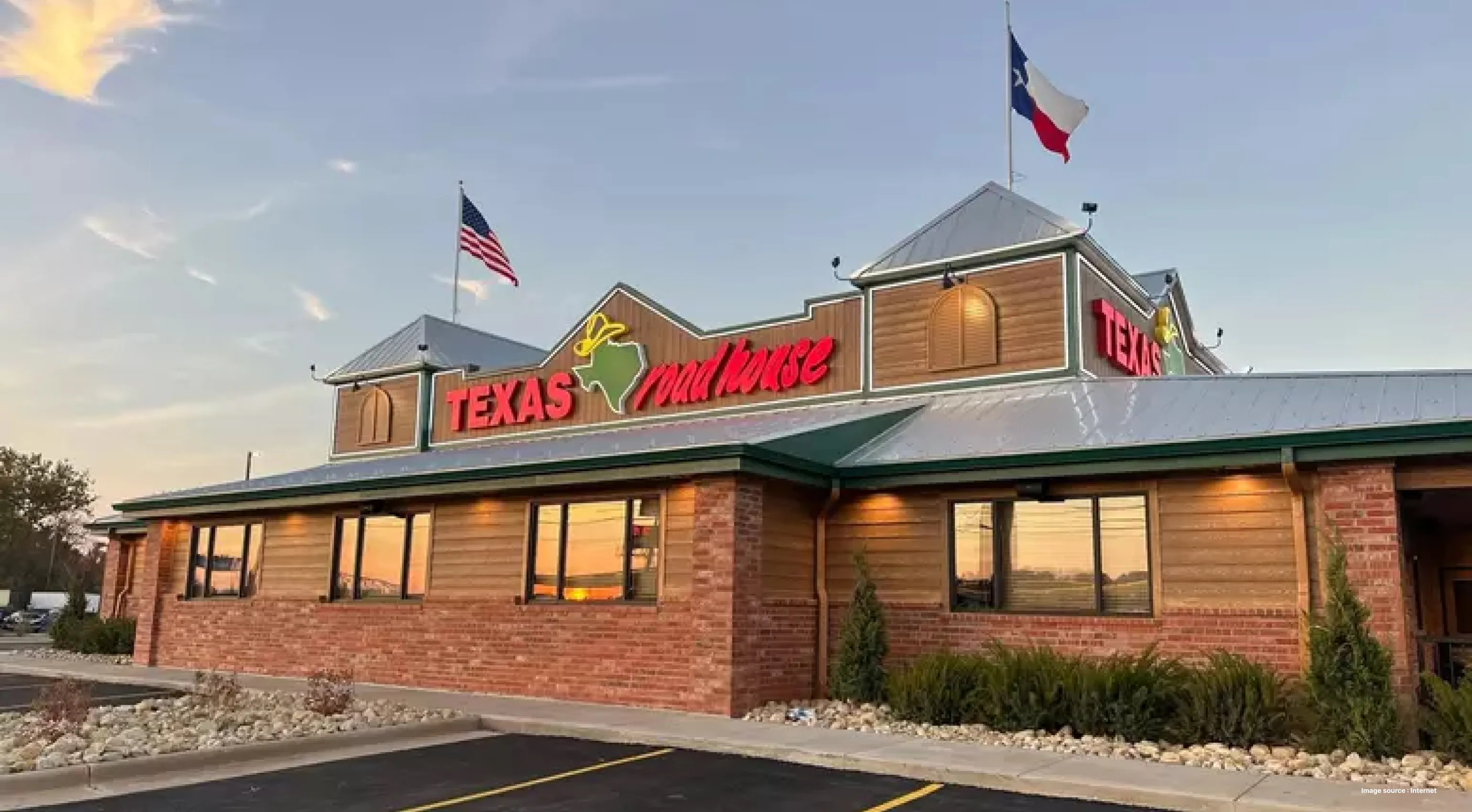 a branch of texas roadhouse restaurant with flags hoisted and a lit up roadsign