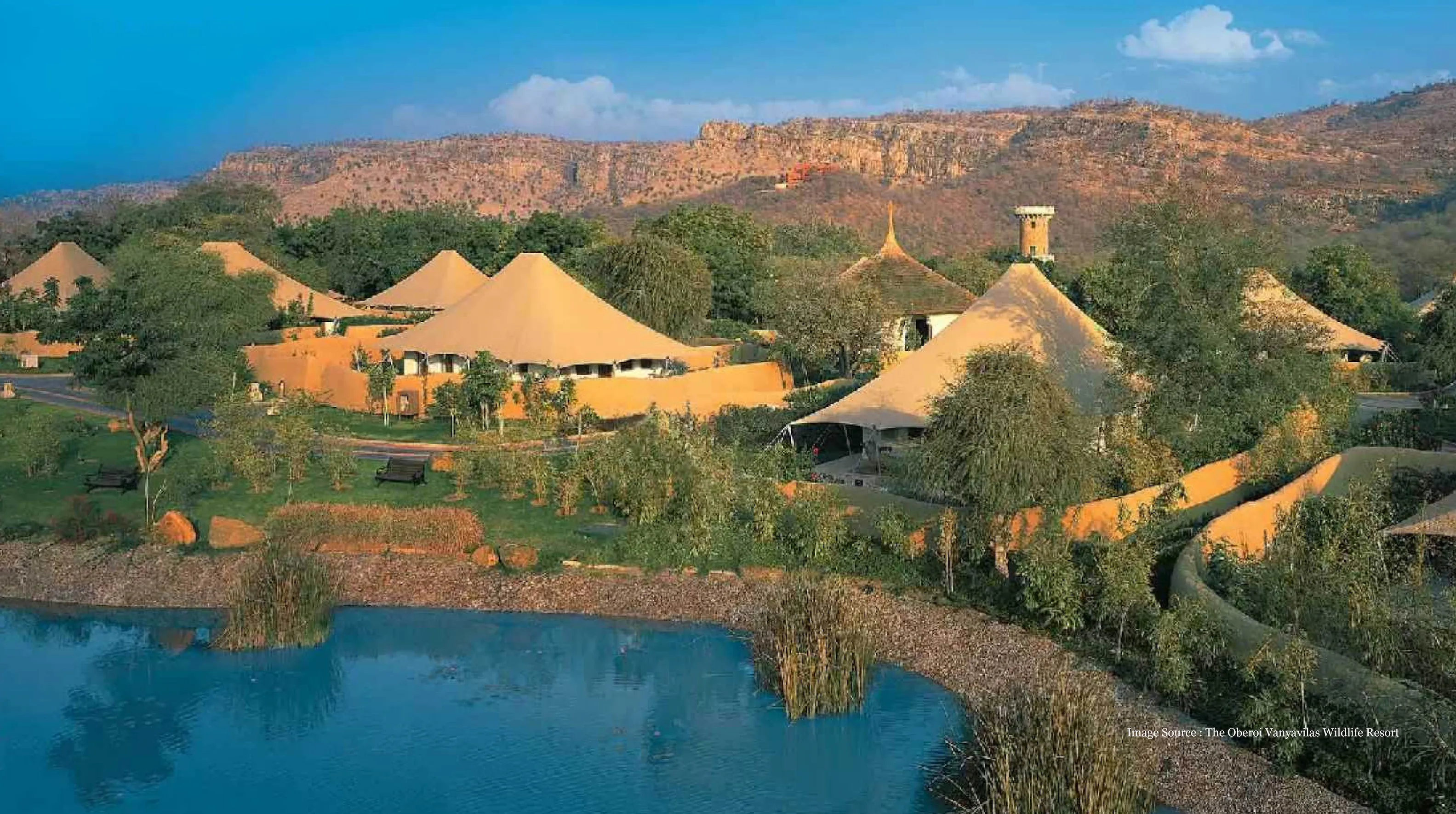 Luxury eco retreat with lavish tented accommodations by a serene pond, surrounded by lush greenery and hills at an exclusive resort
