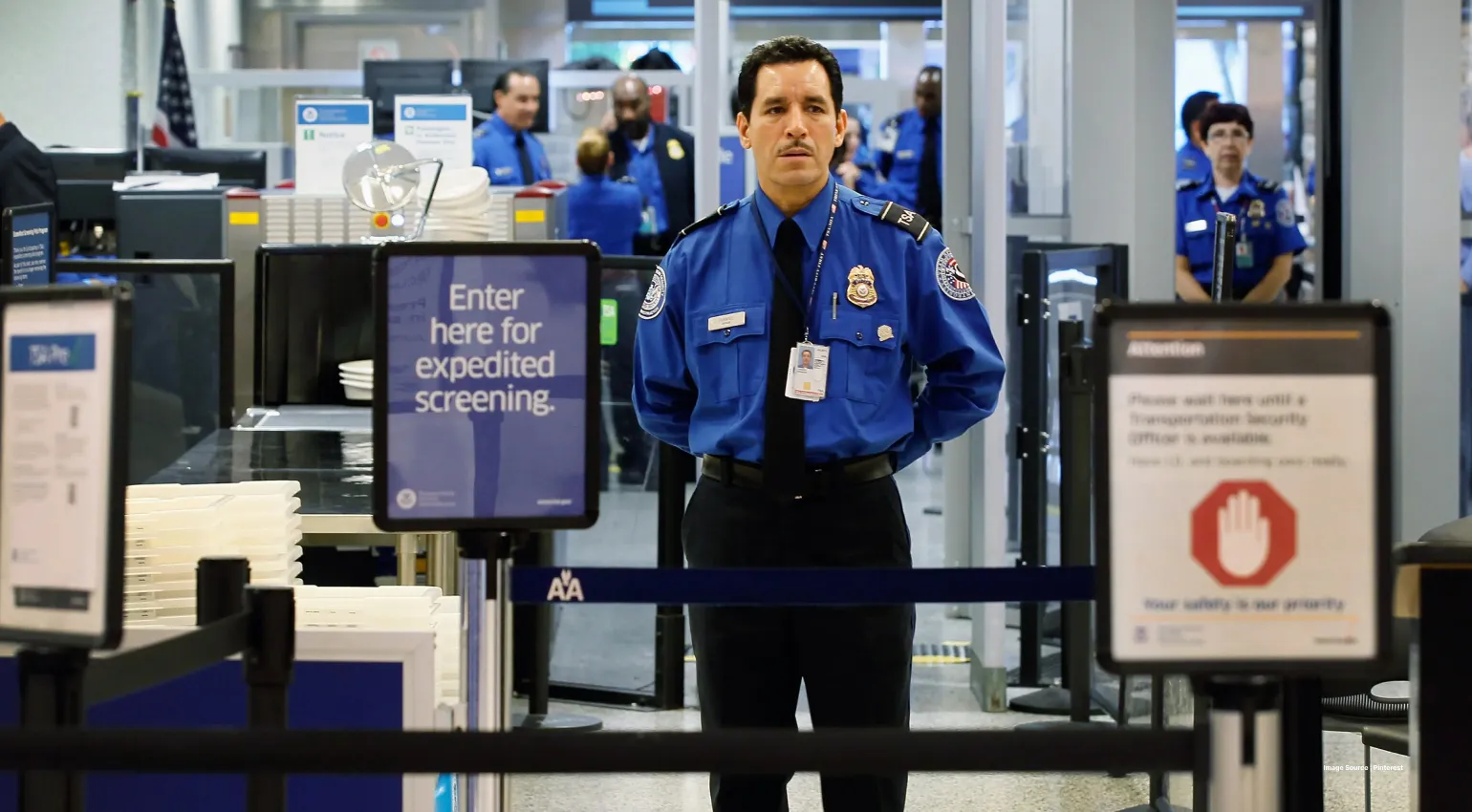 a uniformed security man standing at airport security lane with signboards on either side